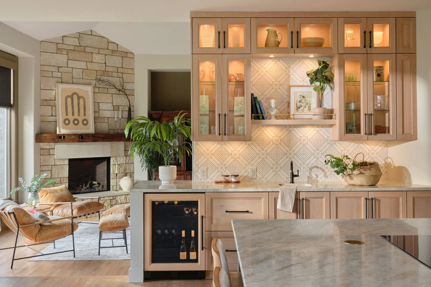 Beverage station with lit glass cabinets and printed marble backsplash, the fireplace beyond