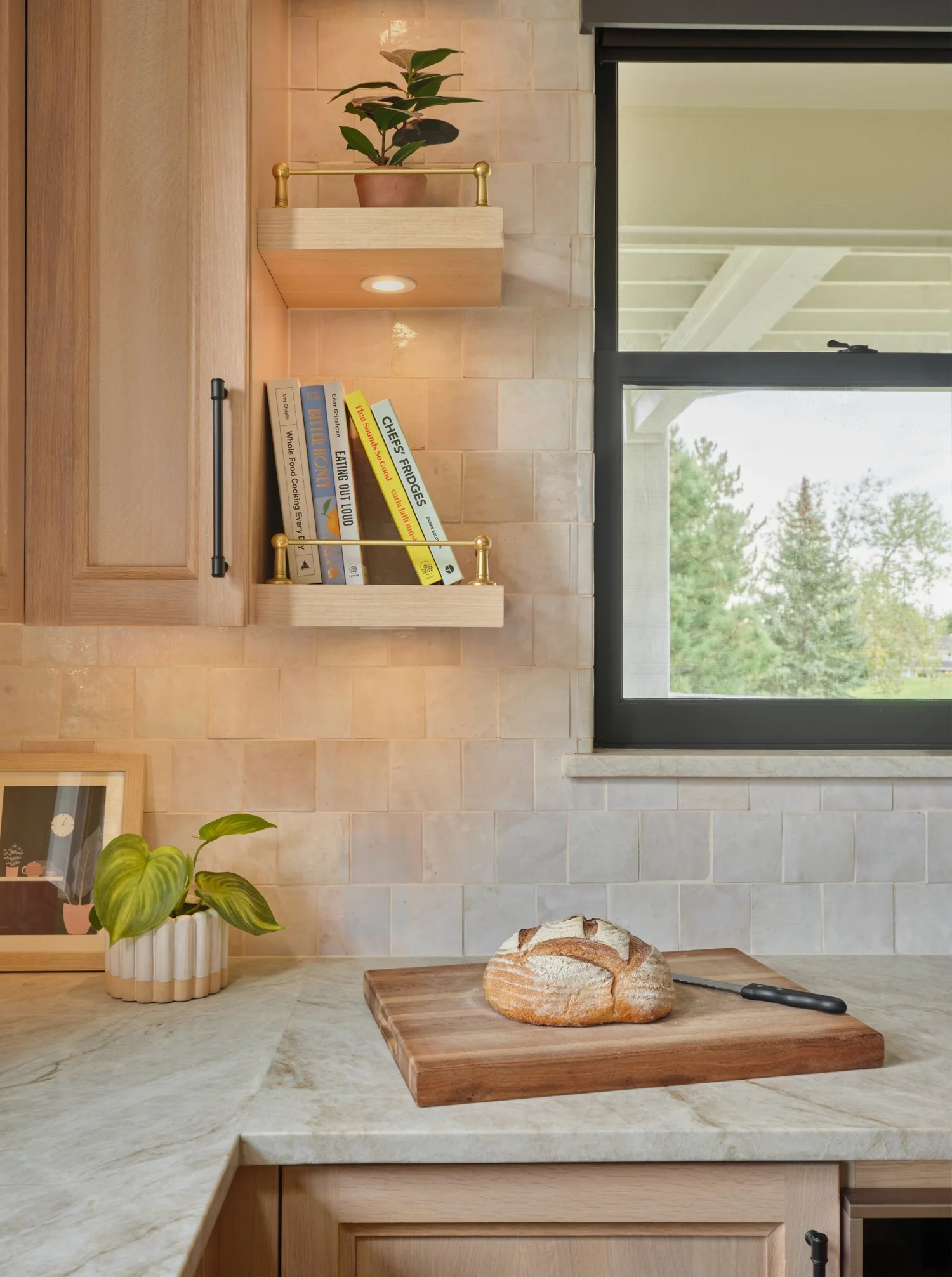 Cookbooks on a floating shelf with a brass rail against pink cast zellige