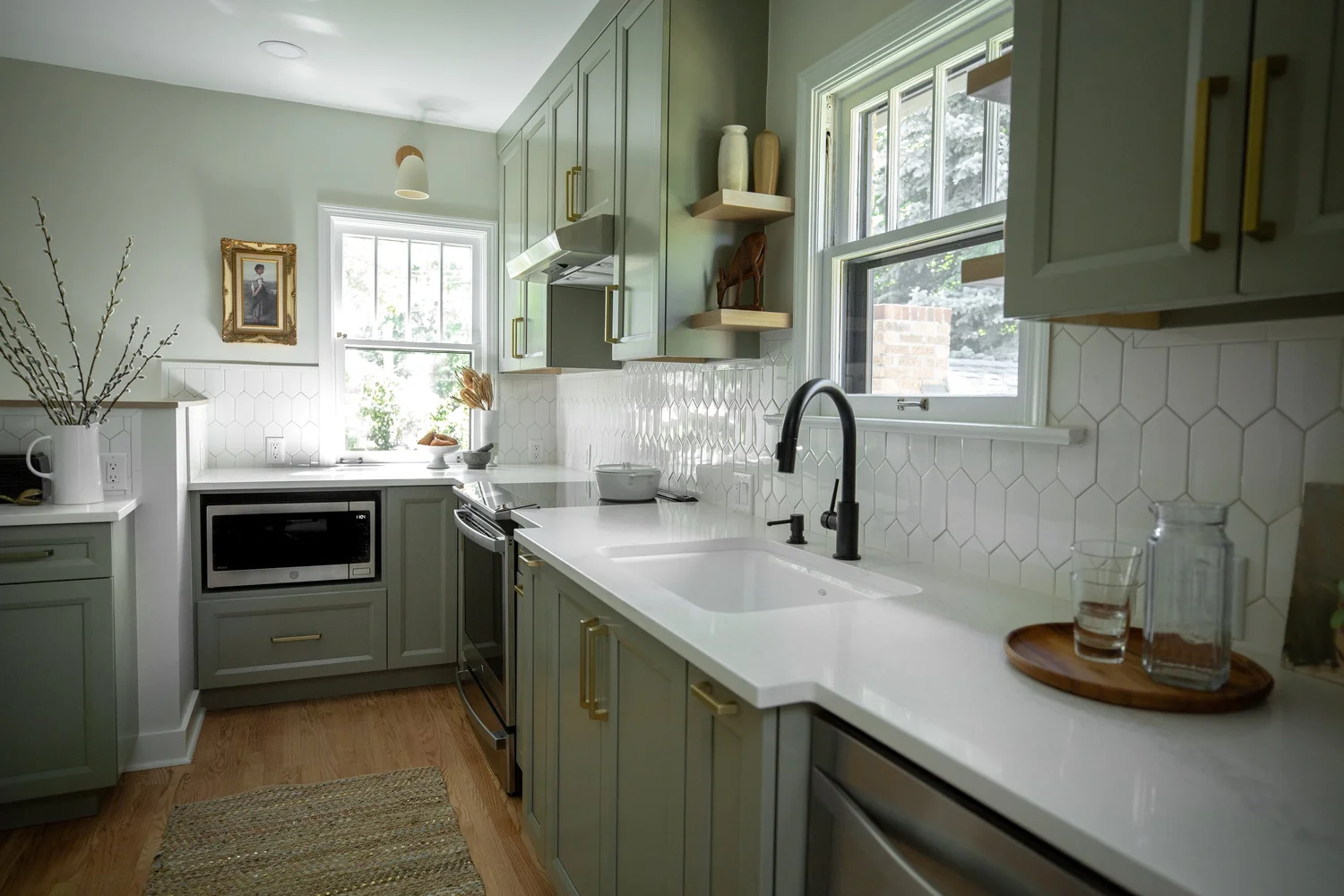 Small kitchen in a historic bungalow with soft green cabinetry, white countertops, and a window over the sink set into a bump-out