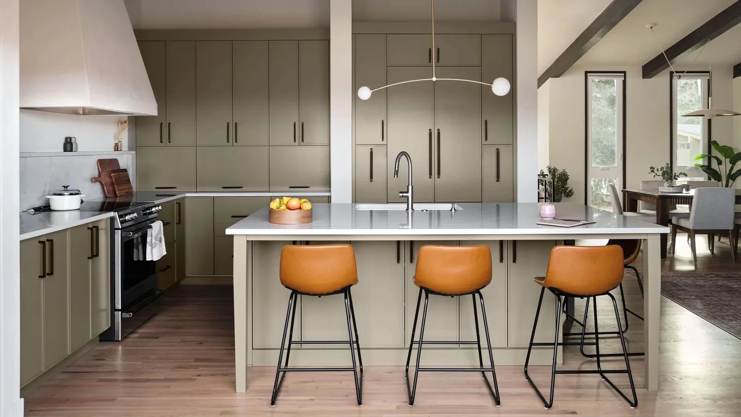 Kitchen with sage green flat-panel cabinets, a large island with a white countertop and cognac leather counter stools, a plaster range hood, and a modern linear pendant light