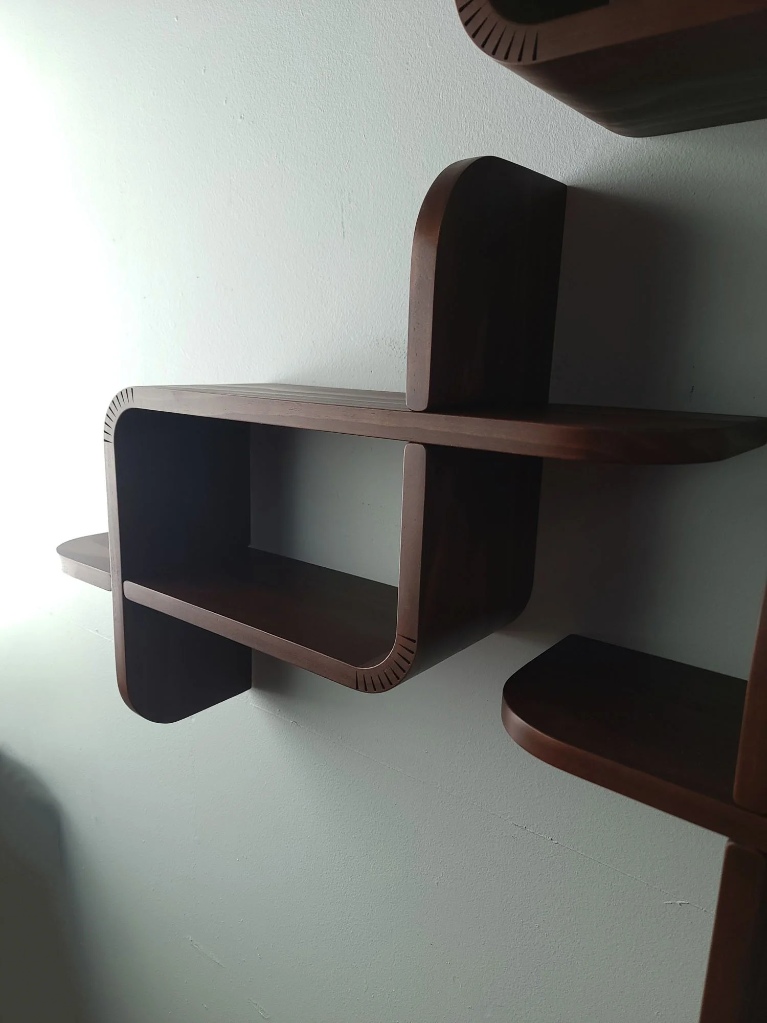 Modern wooden wall-mounted shelf with rounded edges, open compartment, against a light-colored wall.