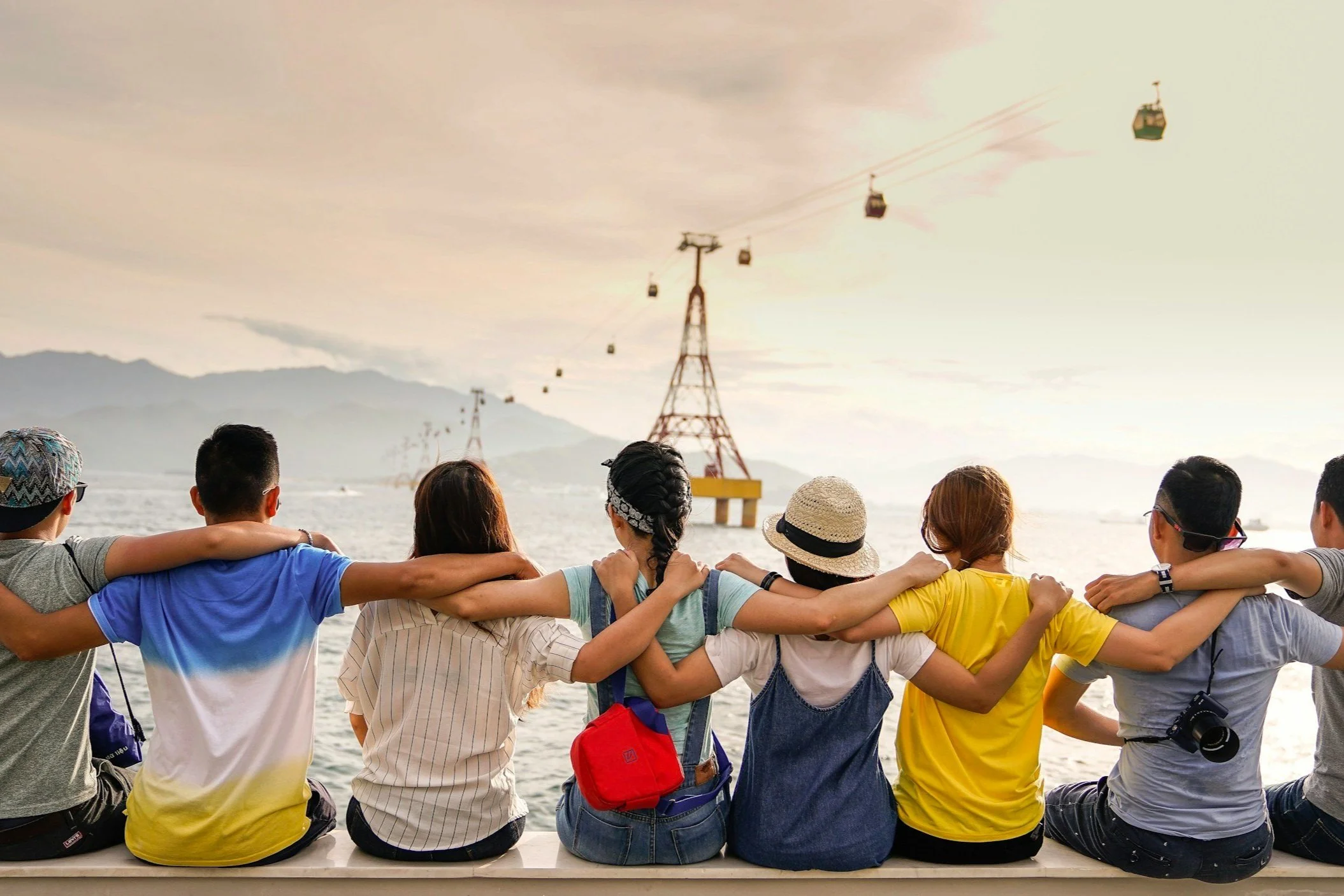 Eight people, seated in a row, arms atop each others shoulders, enjoying a scenic view at golden hour