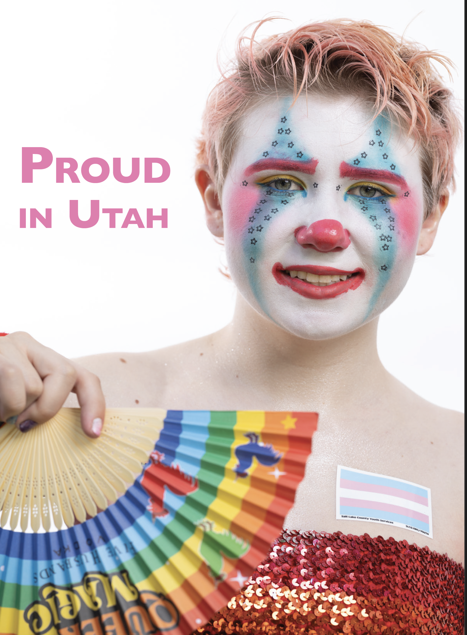 Person with rainbow-colored clown makeup smiling, holding a rainbow fan, wearing a red sequin top, with a Utah state flag sticker on the shoulder, and the text "Proud in Utah" in pink beside them.