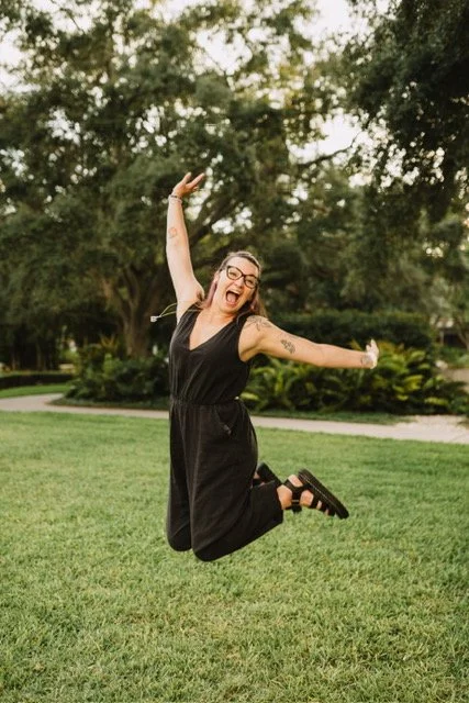Photo of Sarah Parrott in a pink jumpsuit smiling in front of a pretty background of foliage