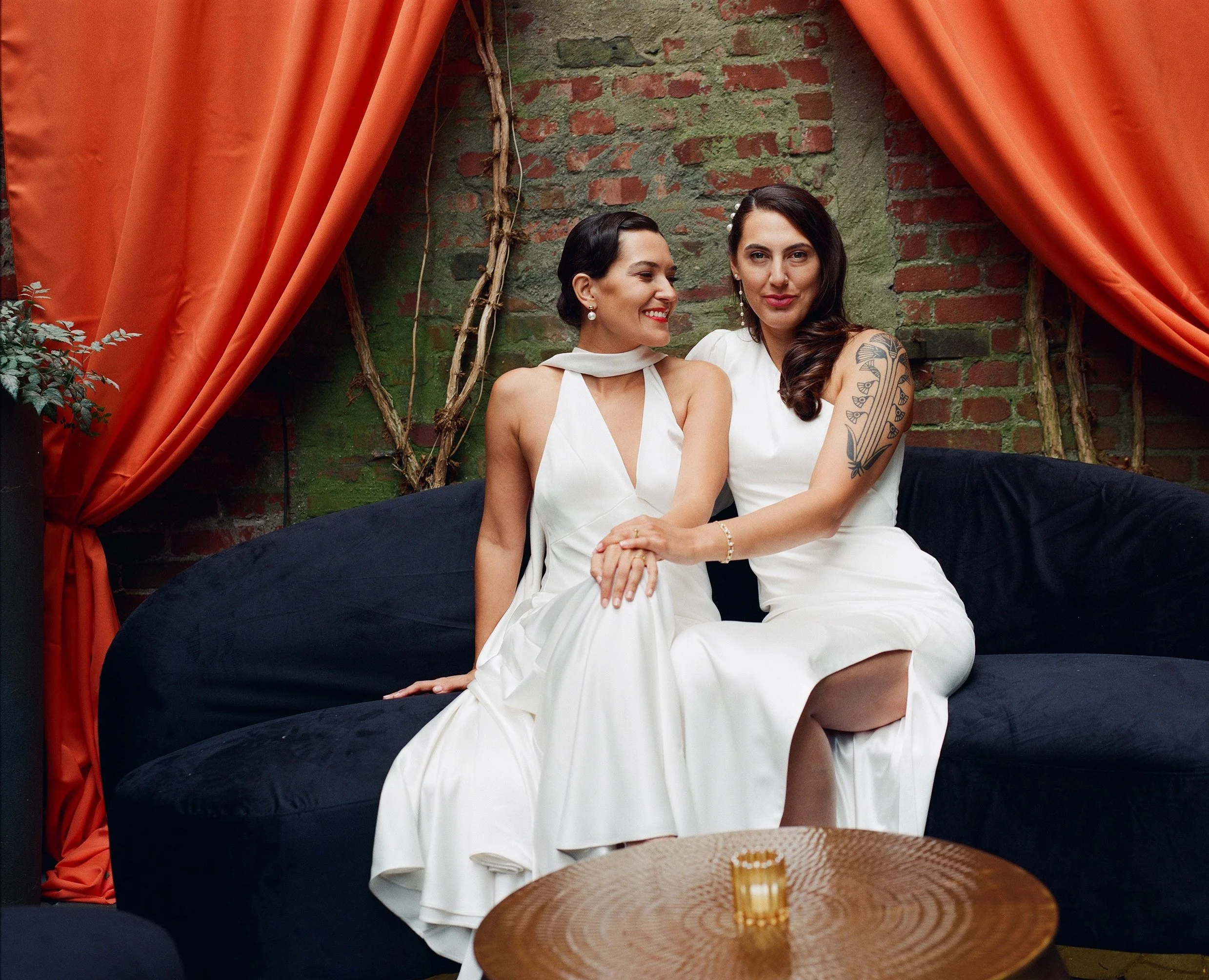 NYC wedding photography, two brides holding hands and sitting on a low couch together