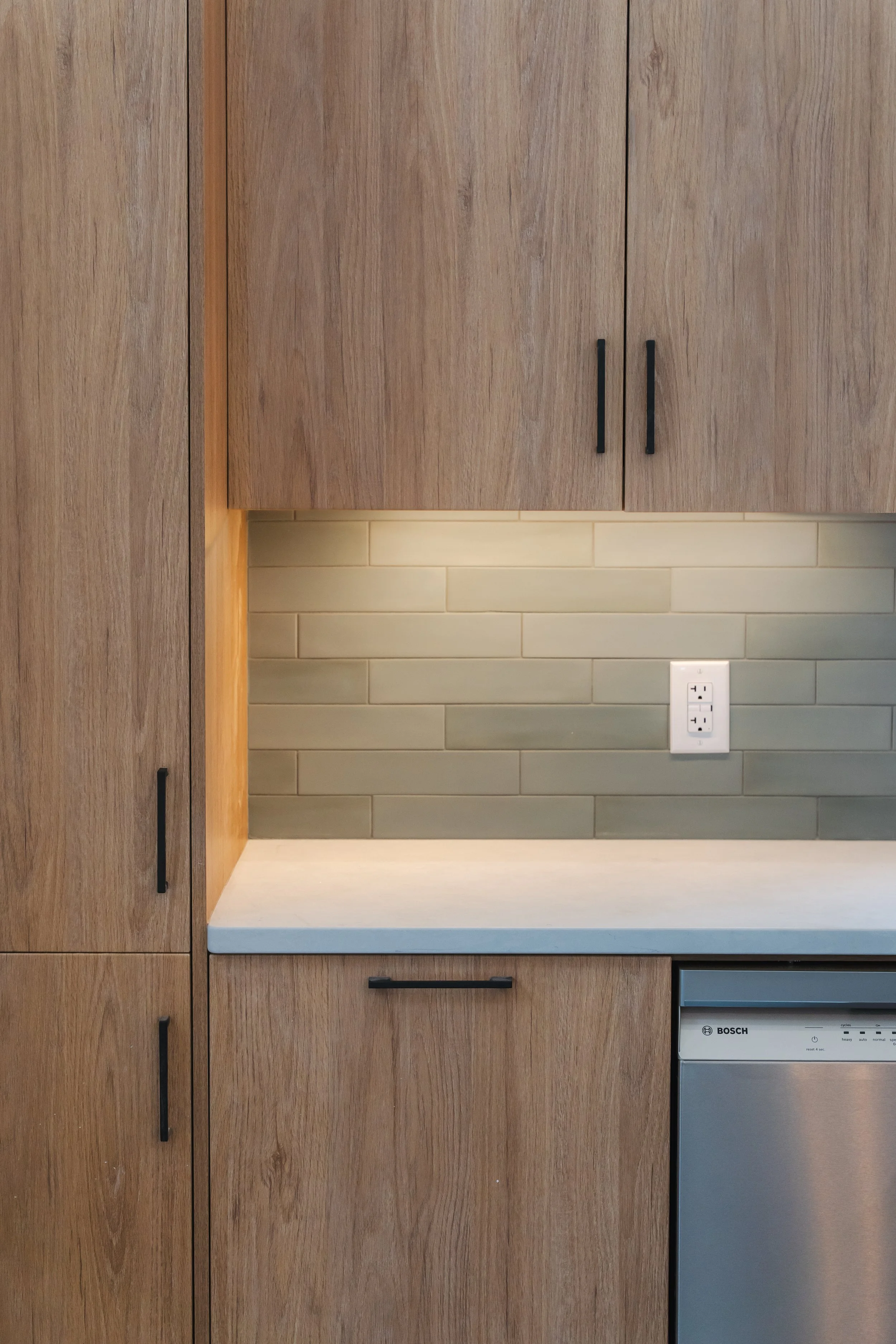 Kitchen countertop with wooden cabinetry, tiled backsplash, and a Bosch dishwasher.