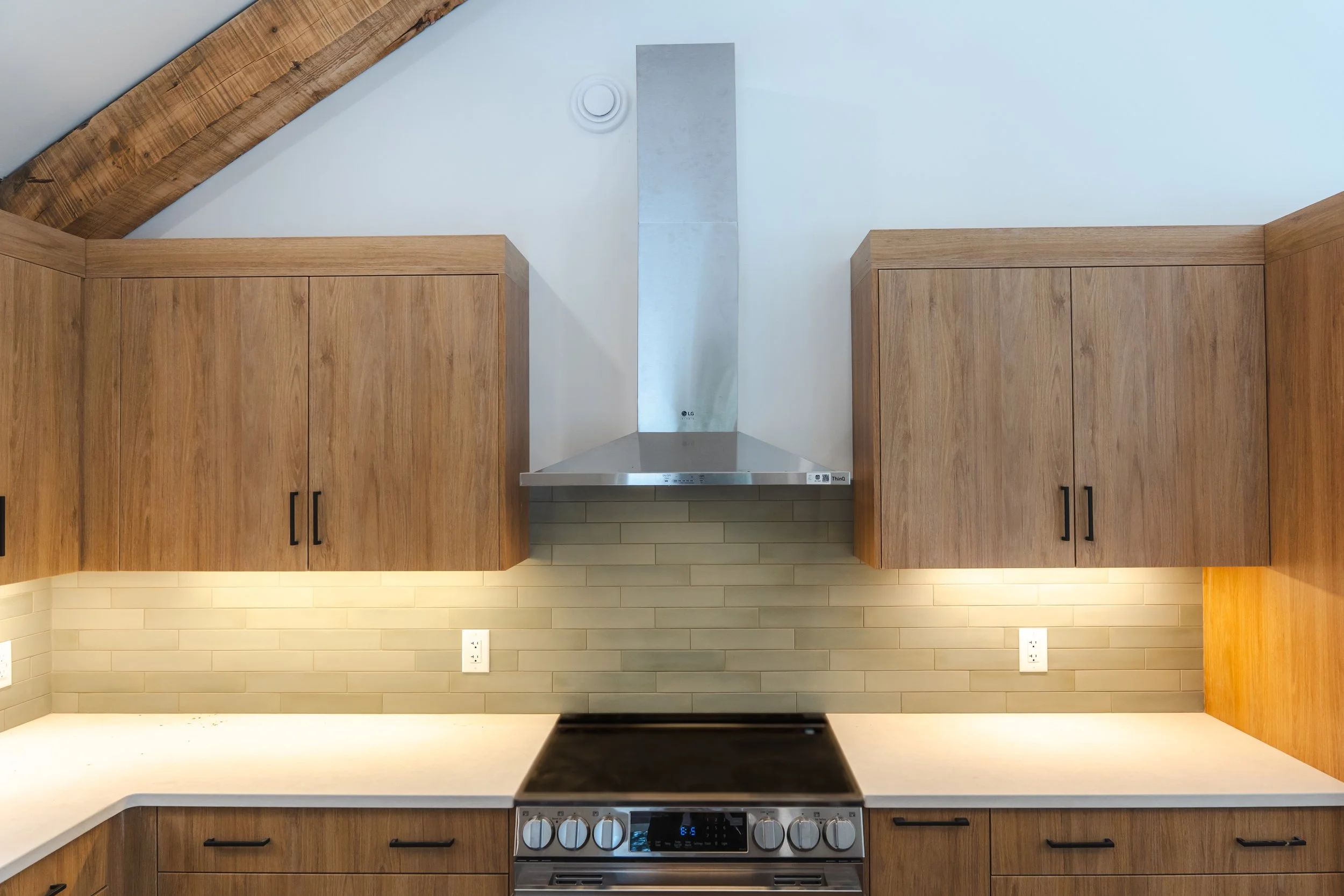 Kitchen with wooden cabinets, a stainless steel stove, a range hood, tiled backsplash, and electrical outlets.