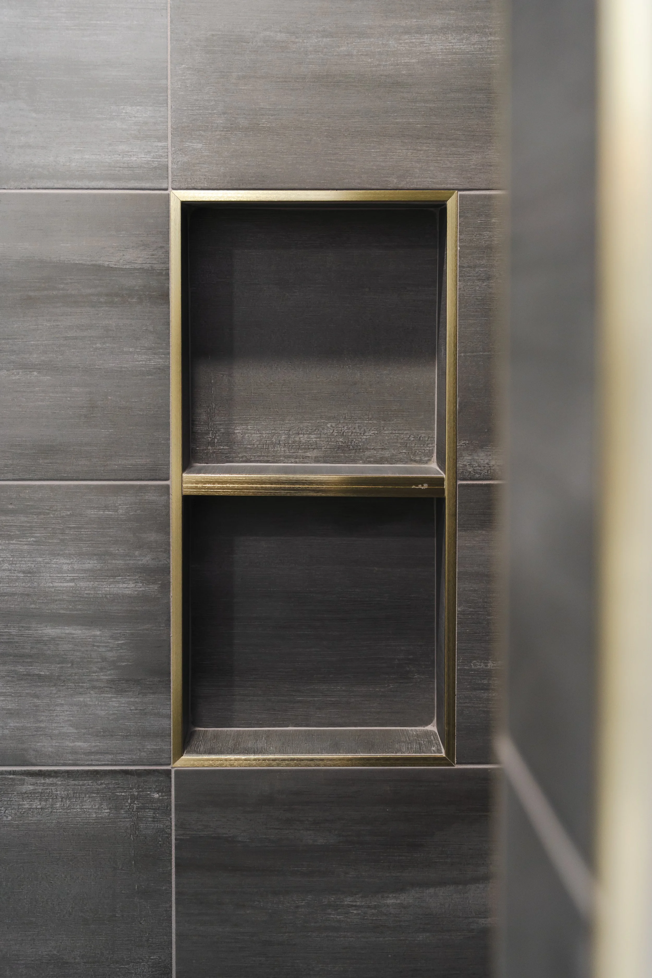 A close-up of a deep wall niche with gold trim, set into gray tiled wall.