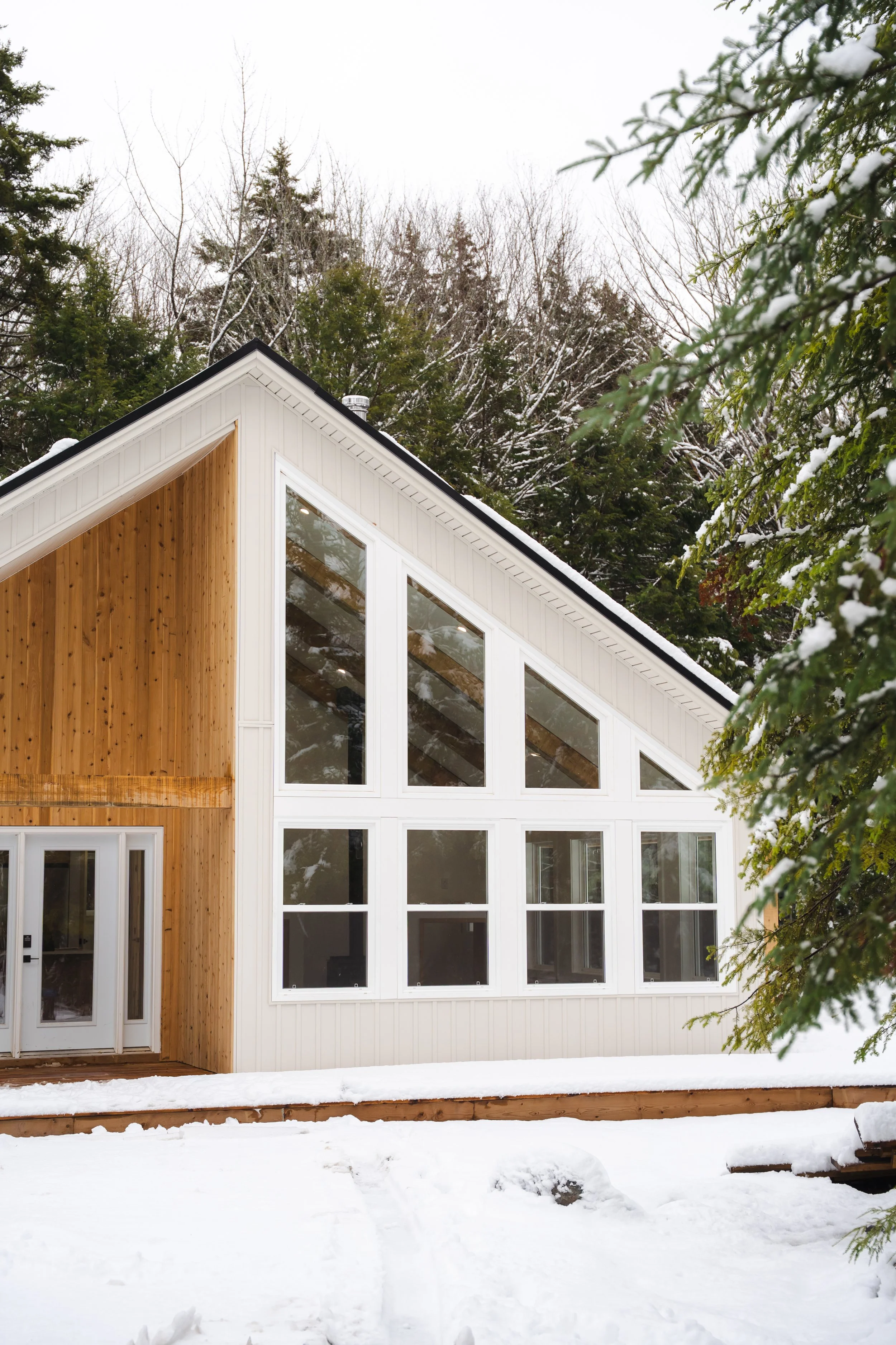 Modern house with large windows and a sloped roof, surrounded by snow and trees.