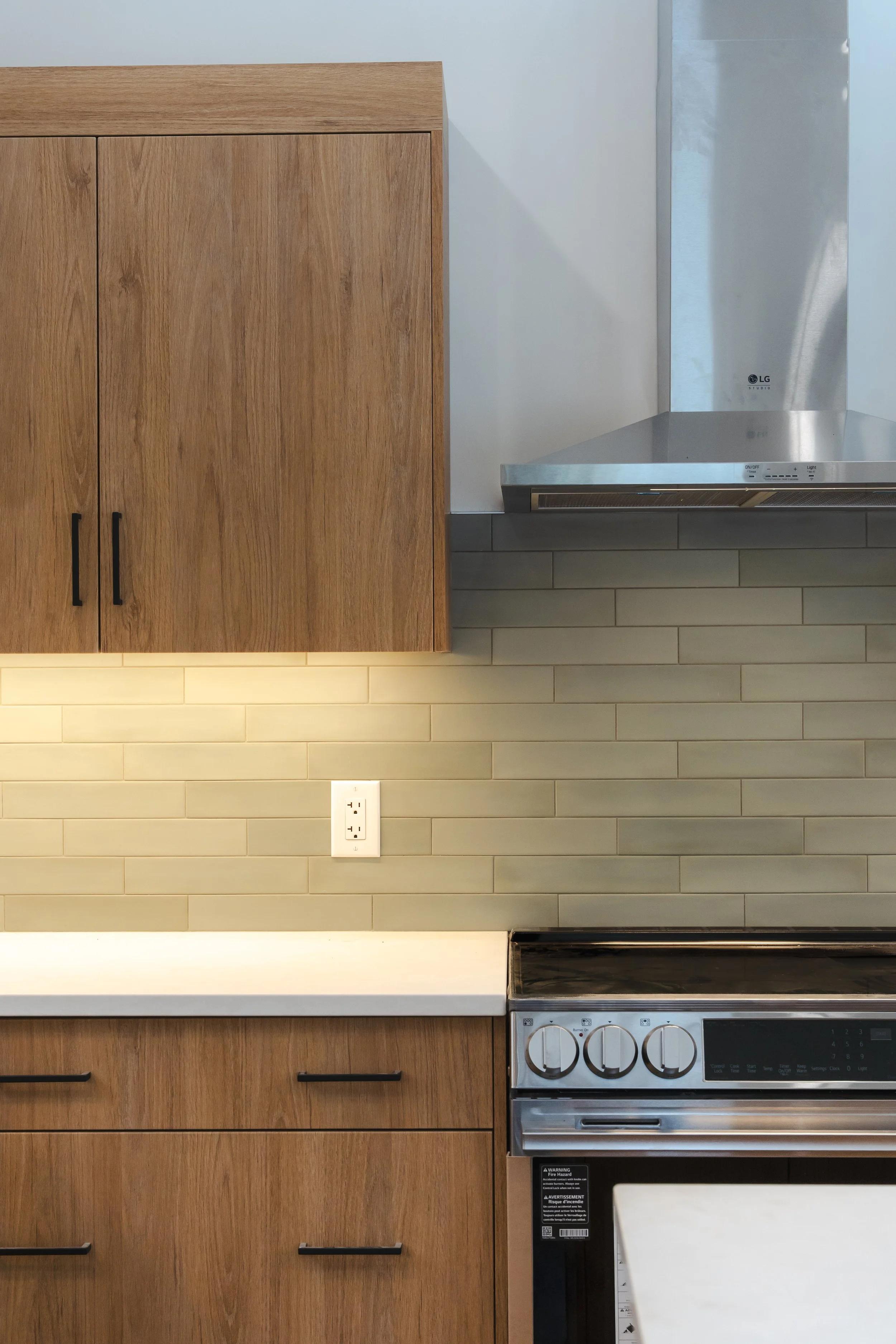 Kitchen with wooden cabinets, a stainless steel range hood, and a black stove, beige tile backsplash, and a white electrical outlet.