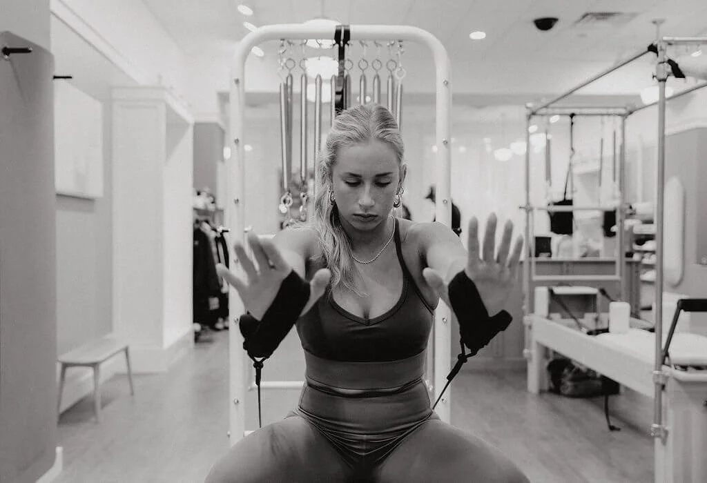 A woman exercising with resistance bands attached to her wrists, in a gym setting.