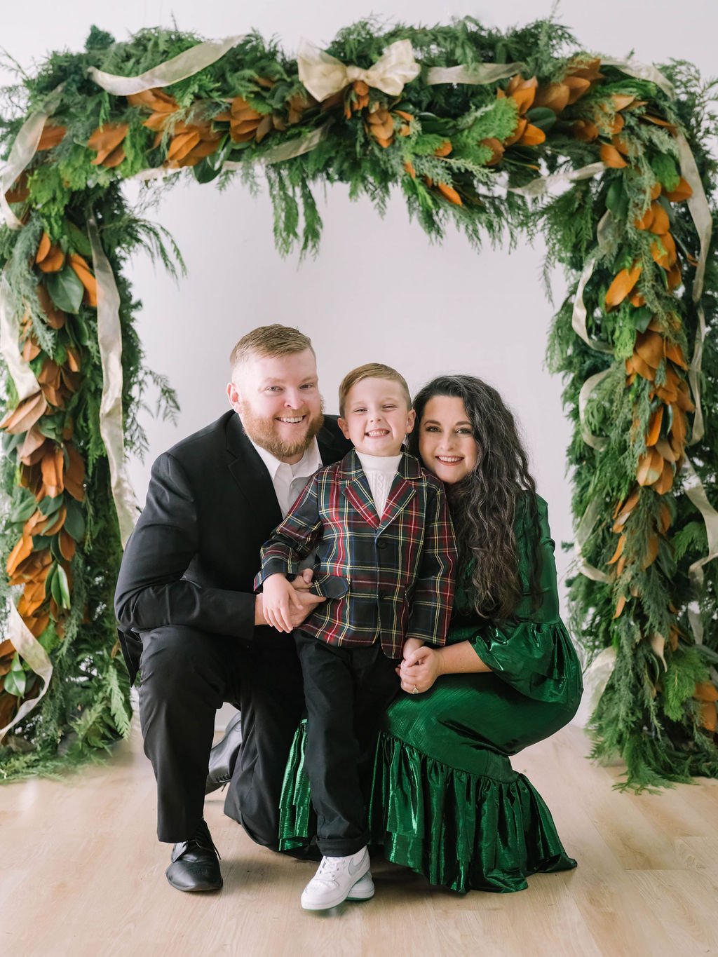 A man, woman, and child posing in front of a decorative greenery arch.
