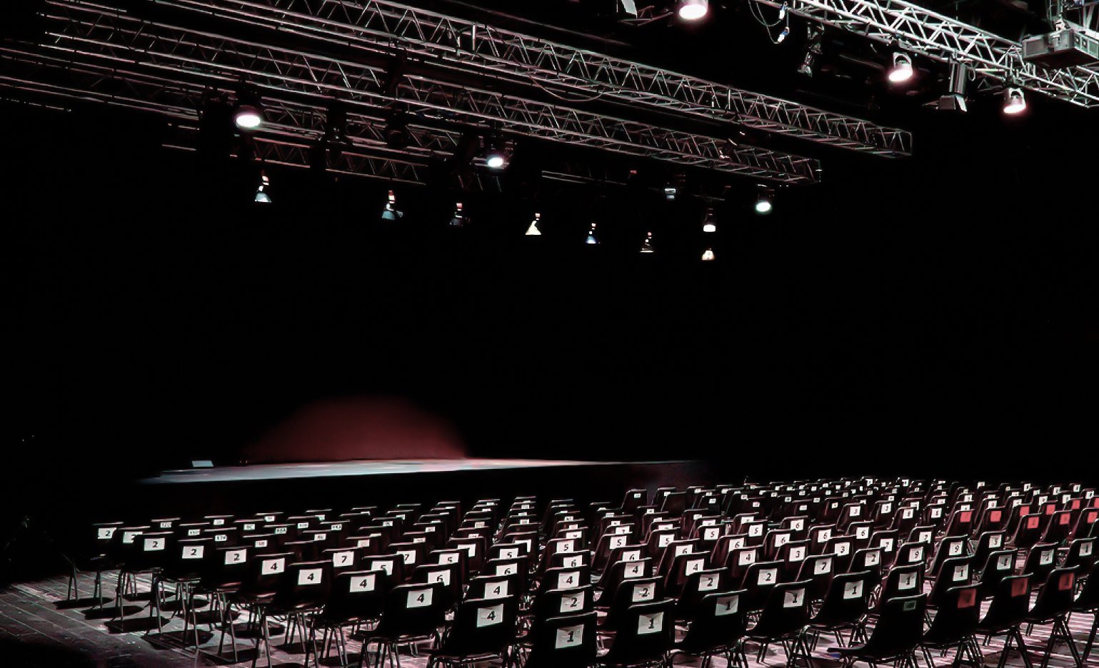 Due persone travestite e con maschere in un teatro, uno con maschera bianca e barba e l'altro con maschera verde e capelli arruffati, mentre recitano una scena.