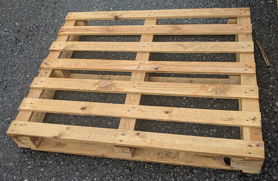 A wooden pallet lying on a gravel surface.