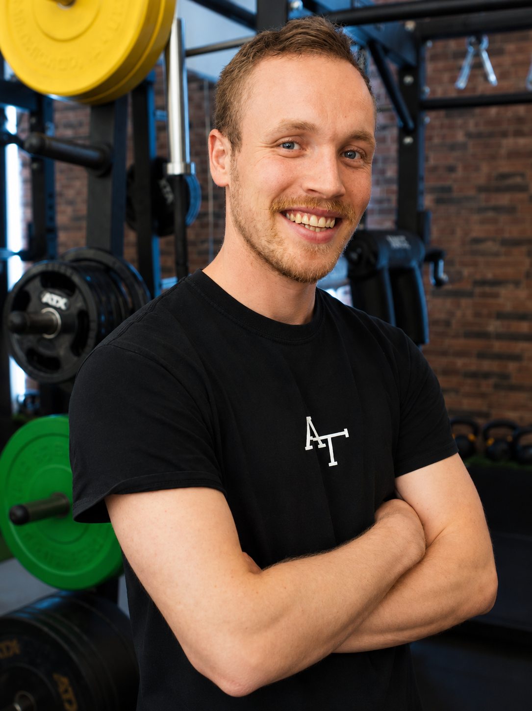 Ein junger Mann in einem Fitnessstudio, in dem Hanteln und Gewichtsscheiben zu sehen sind.