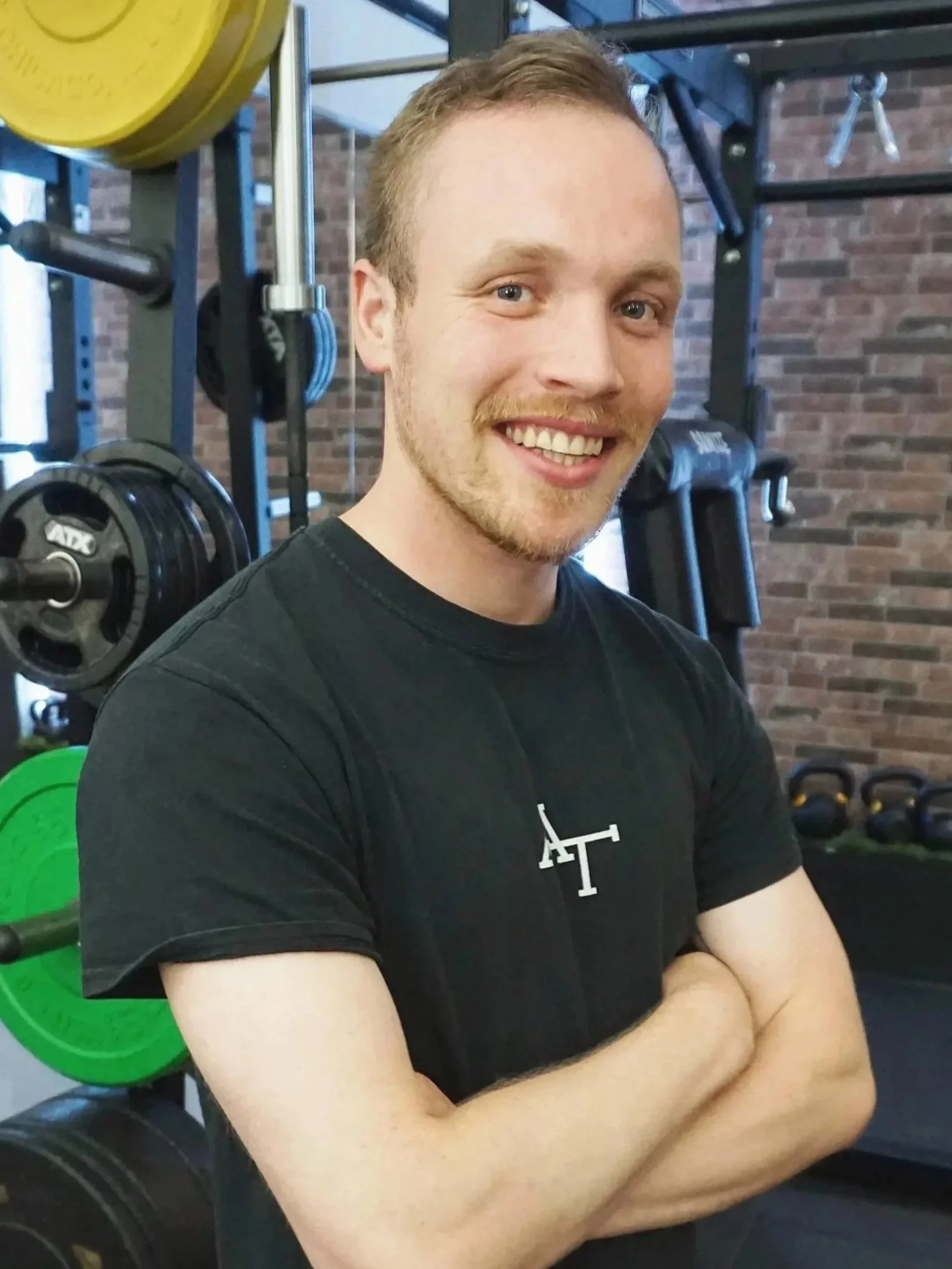 Ein junger Mann in einem Fitnessstudio, in dem Hanteln und Gewichtsscheiben zu sehen sind.