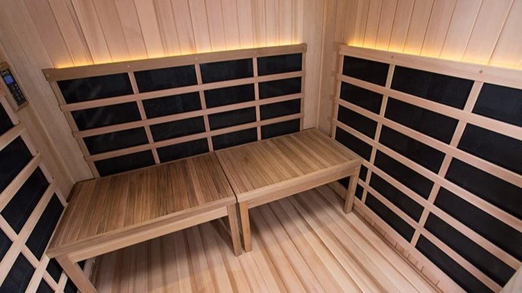 Interior of a small wooden sauna with light-colored wood paneling and black accents, featuring a corner bench.