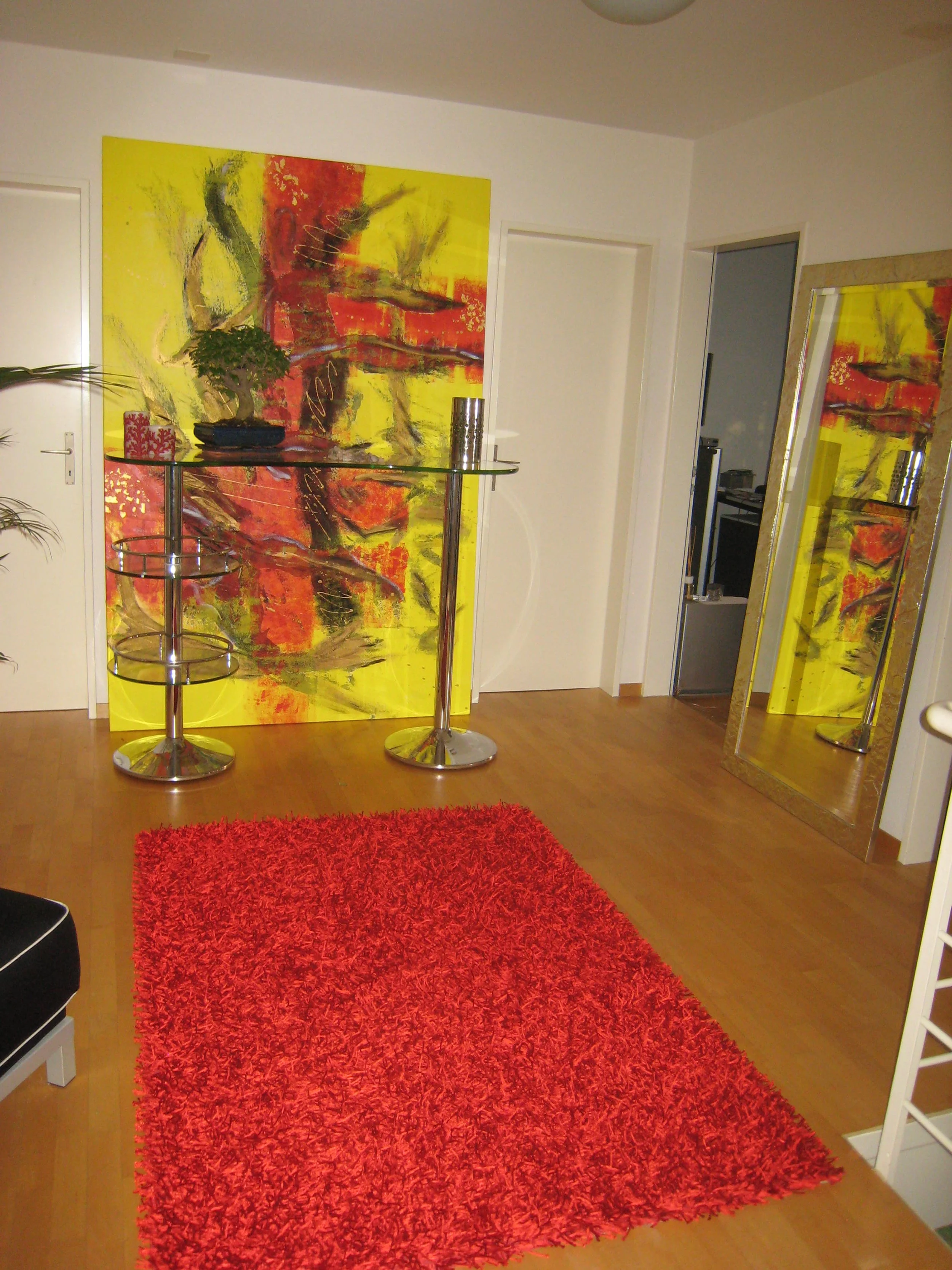 Moderner Wohnzimmerbereich mit einem roten Teppich, einer großen bunten abstrakten Wandkunst, einem Spiegel und einem kleinen Bar-Tisch. Kunst, Gemälde.