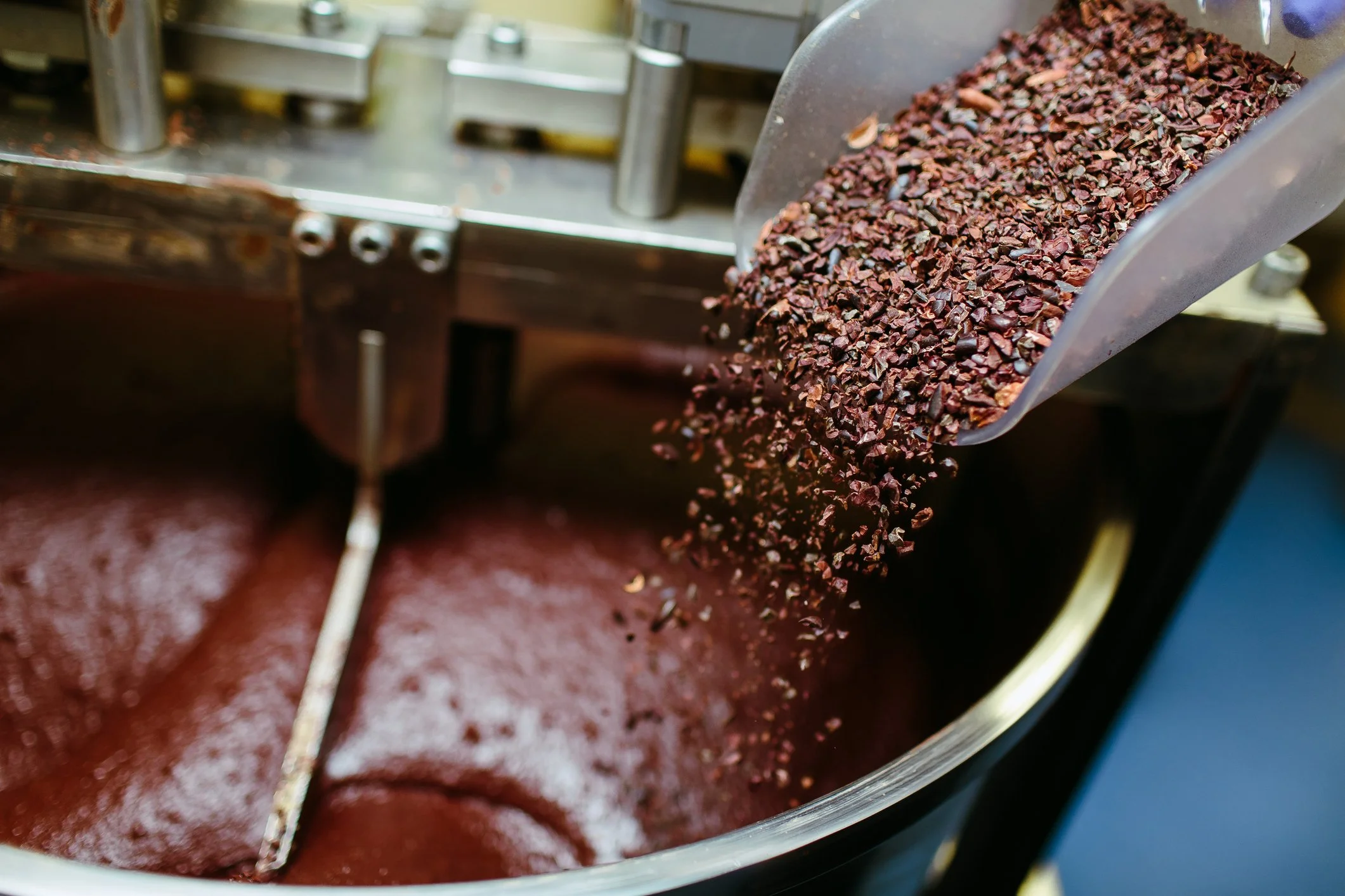 Cocoa nibs pouring into a melanger of liquid chocolate