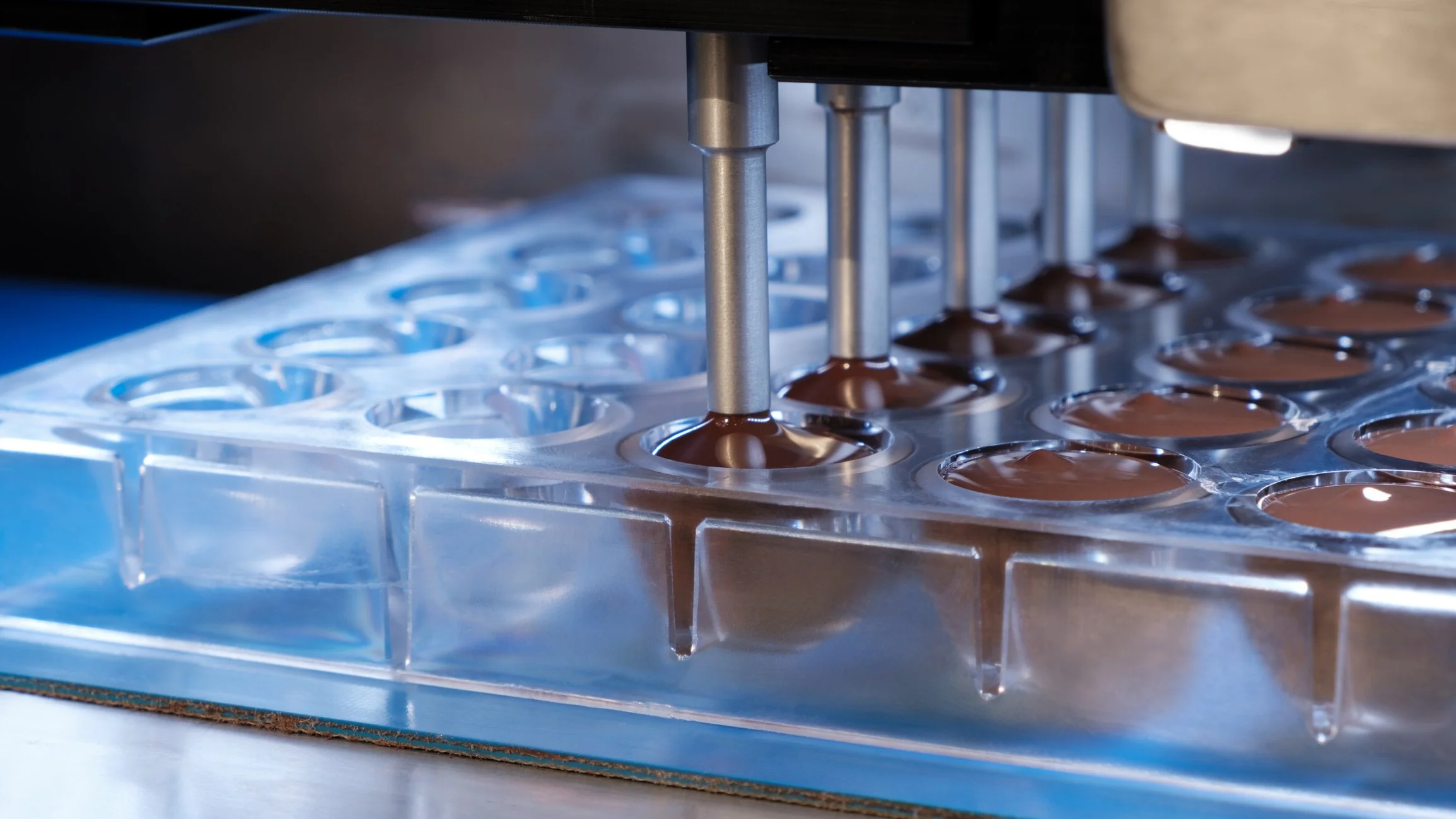 Depositor nozzles filling chocolate molds on a production line
