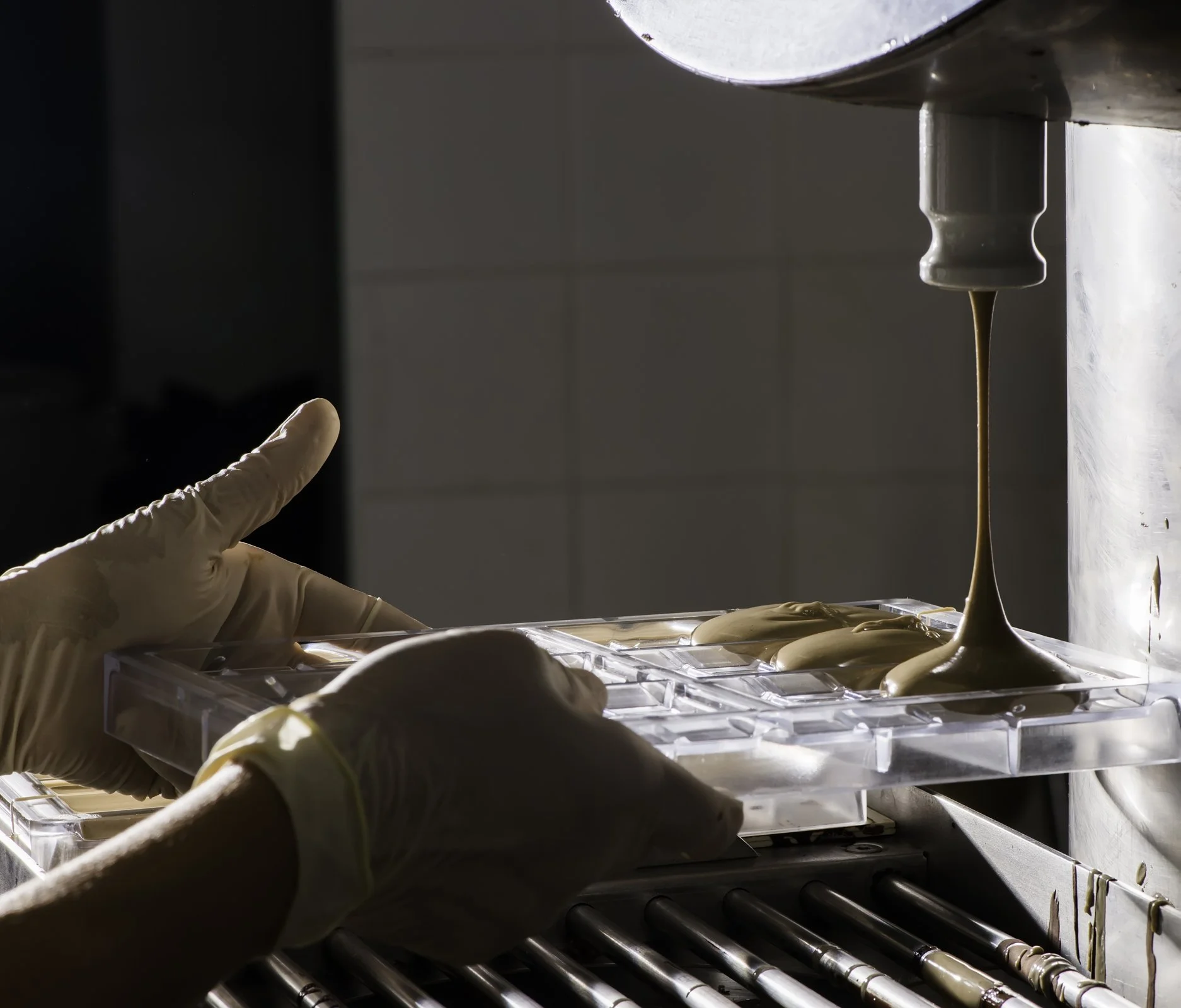 Gloved hand filling a chocolate mold from a depositor nozzle