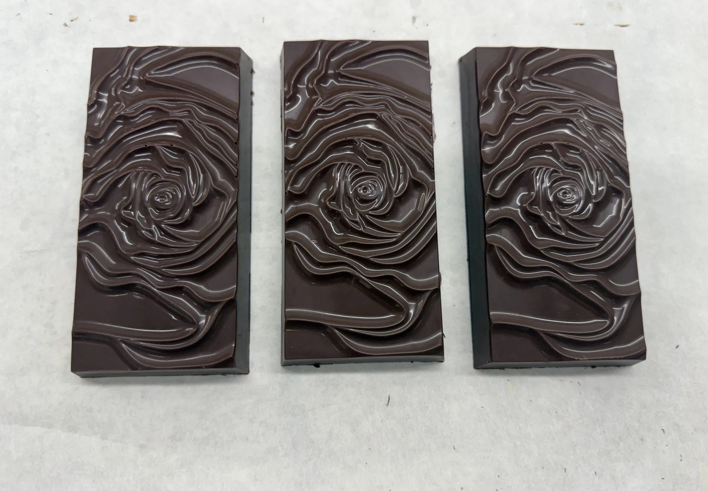 Three dark chocolate bars with a rose pattern molded into the surface