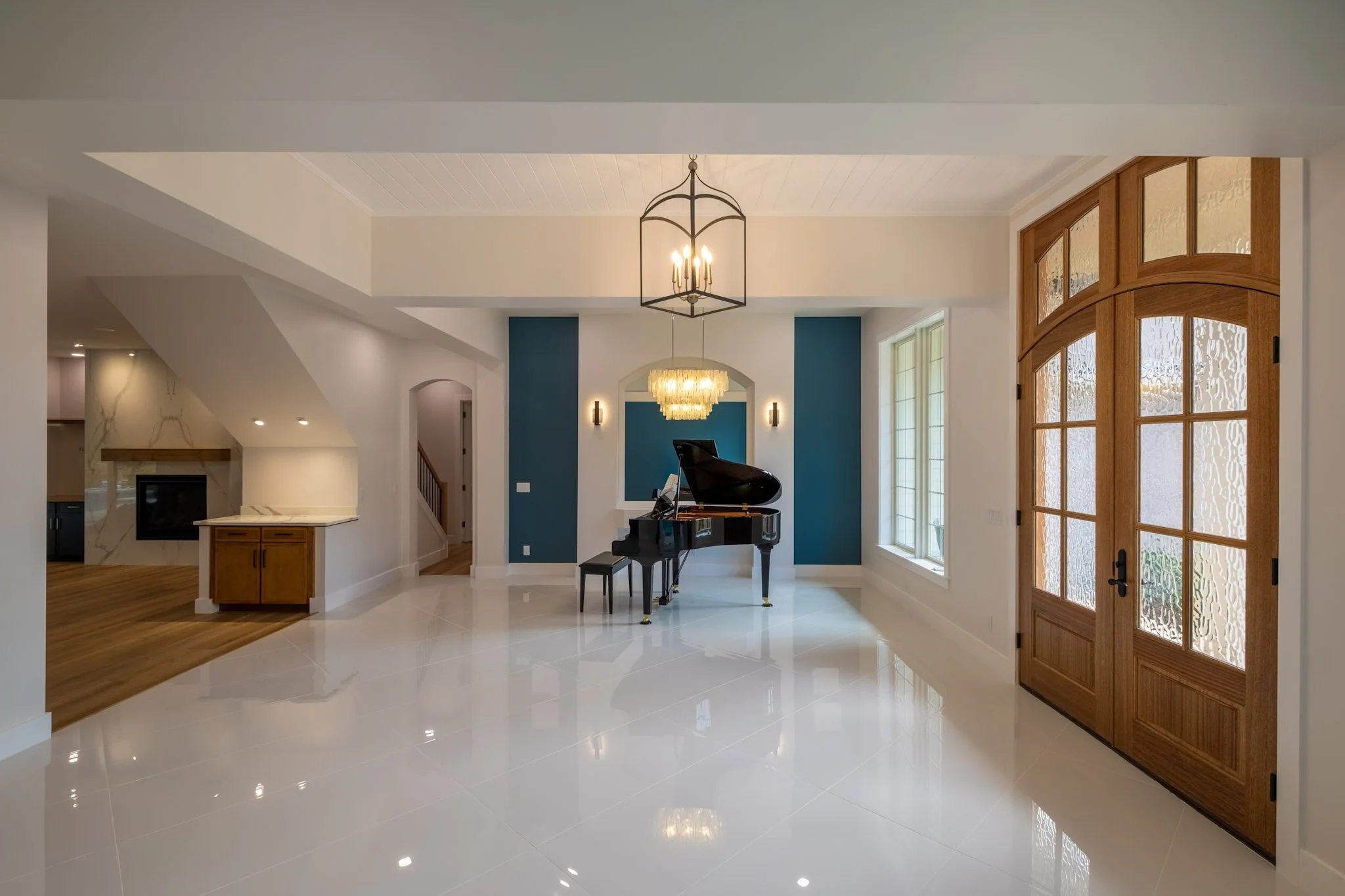 Living room with a black grand piano, white tiled floor, blue accent wall, and a wooden front door with glass panels.