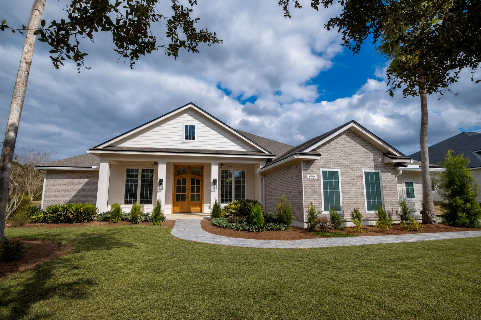 Front view of a modern single-family house with a landscaped lawn, paved walkway, and a partly cloudy sky.