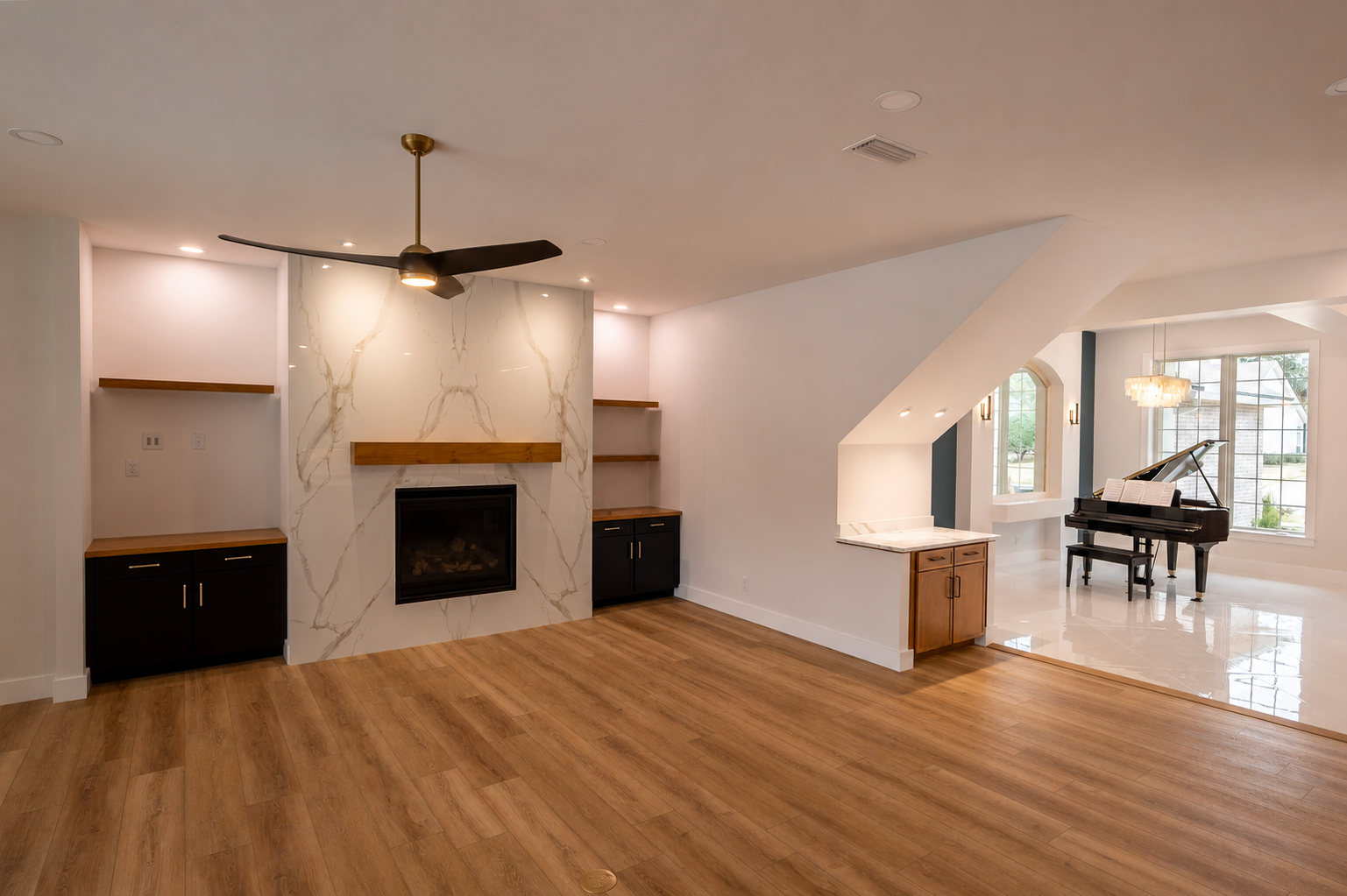 Living room with wooden floor, fireplace with marble finish, built-in shelves, ceiling fan, and a grand piano near large windows.