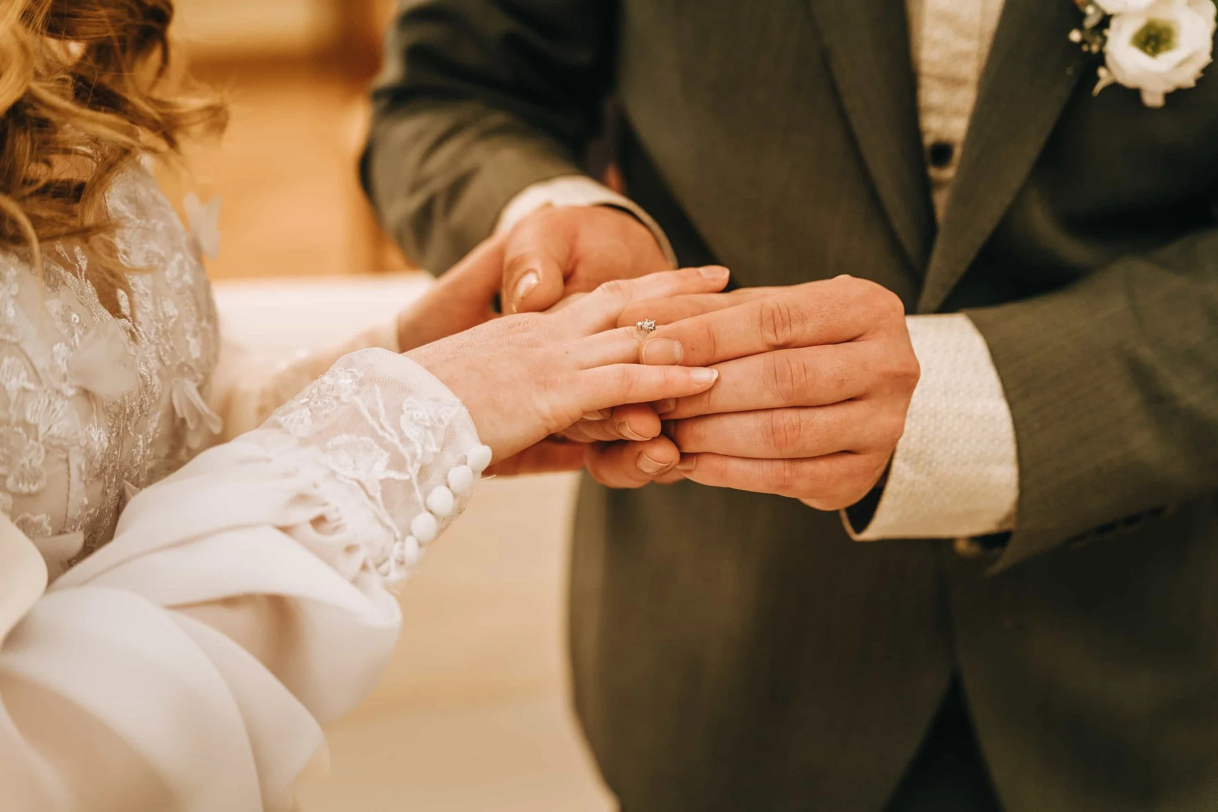 Ringtausch bei der Hochzeit, Nahaufnahme der Hände mit Spitzendetails am Brautkleid