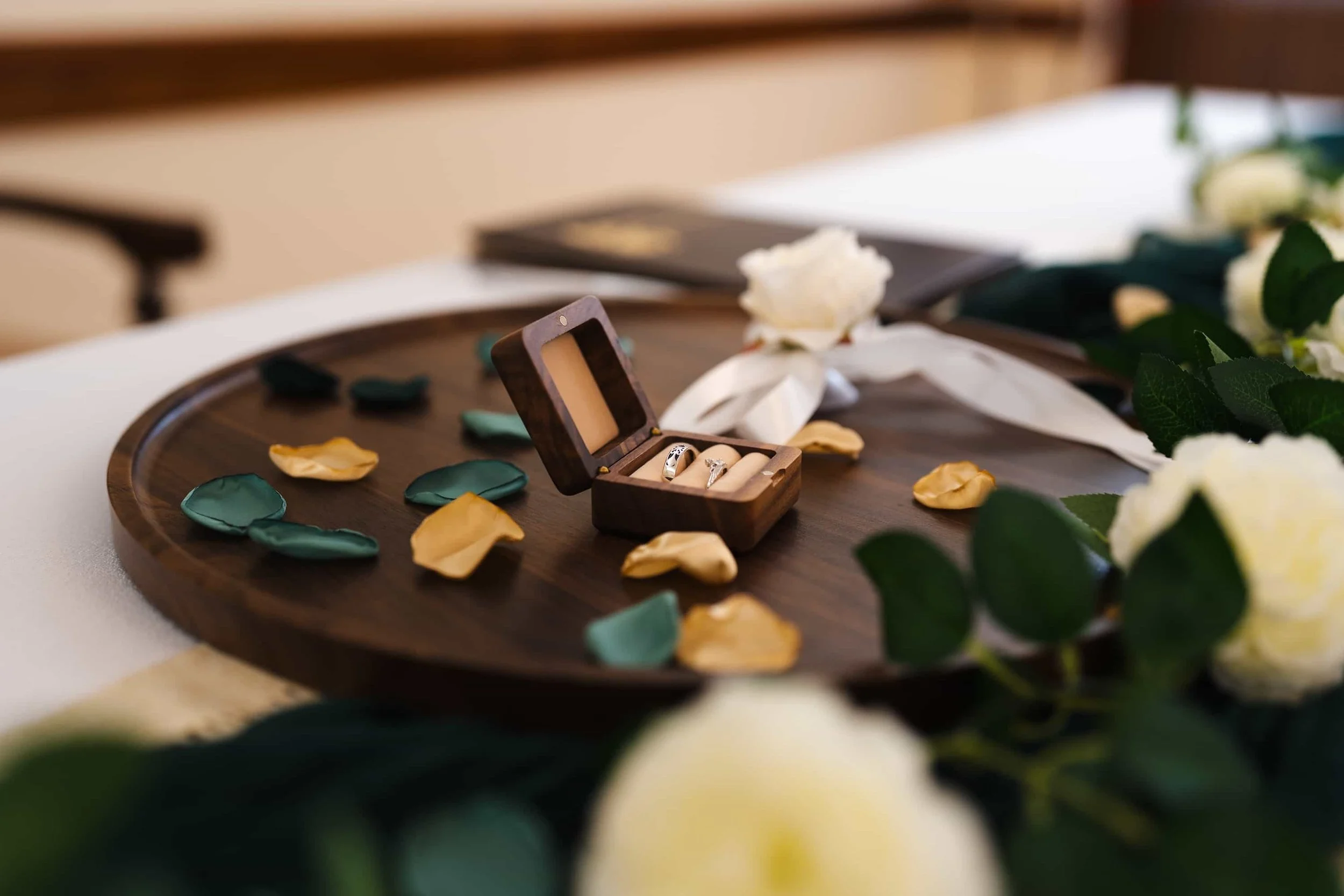 Hochzeitsdekoration mit Ringbox auf einem Holztablett, weiße Rosen und Blütenblätter als Tischdeko