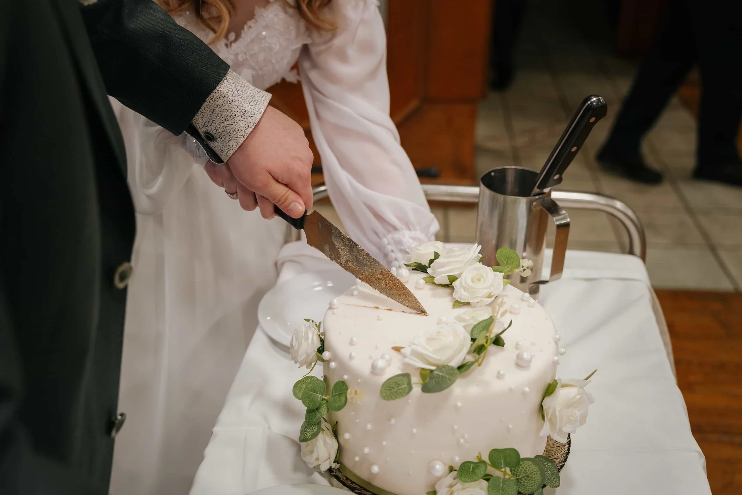 Tortenanschnitt bei der Hochzeitsfeier, zweistöckige weiße Hochzeitstorte mit weißen Rosen und Eukalyptus