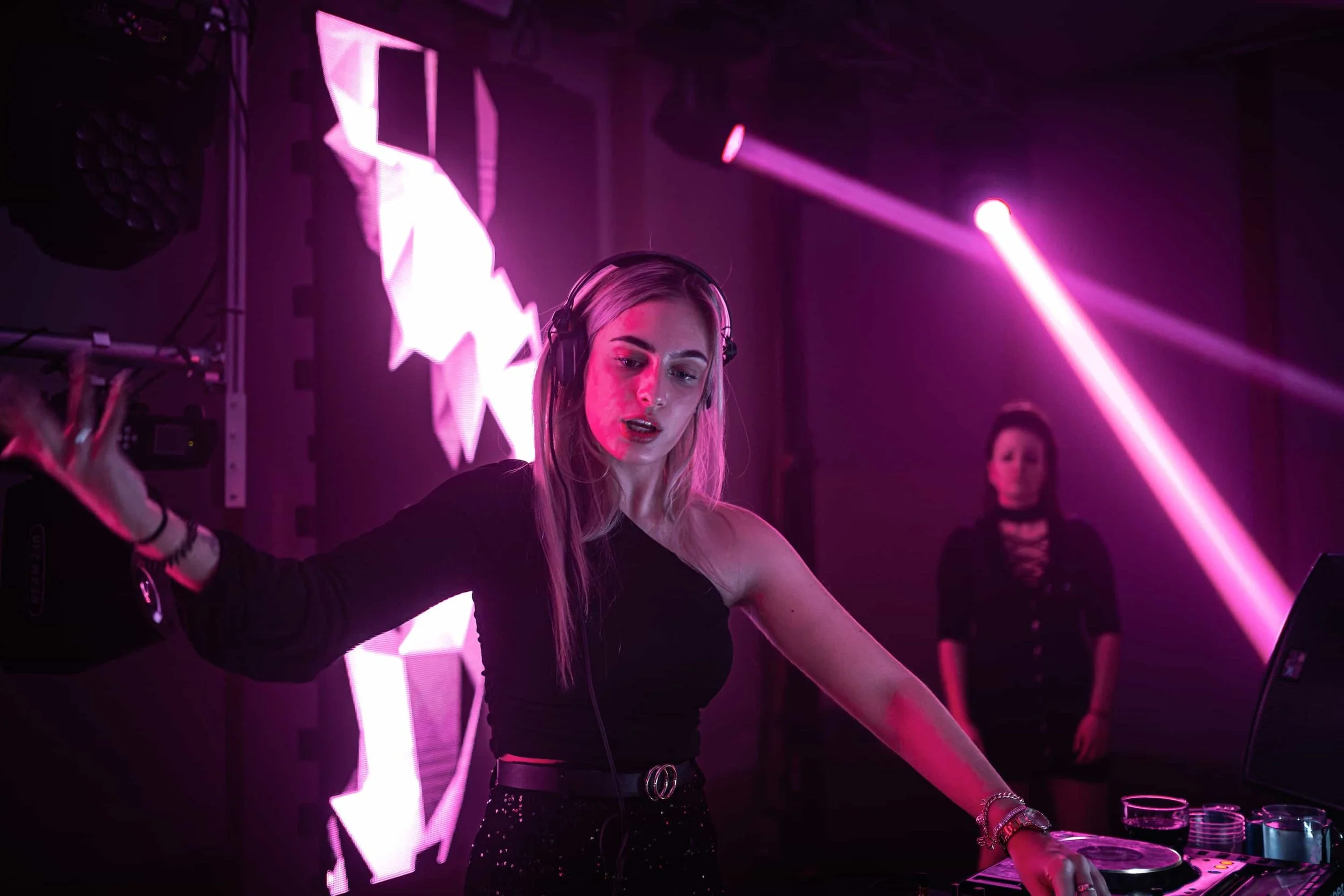 DJ an den Turntables bei einer Abendveranstaltung, beleuchtet von pinken Bühnenlichtern