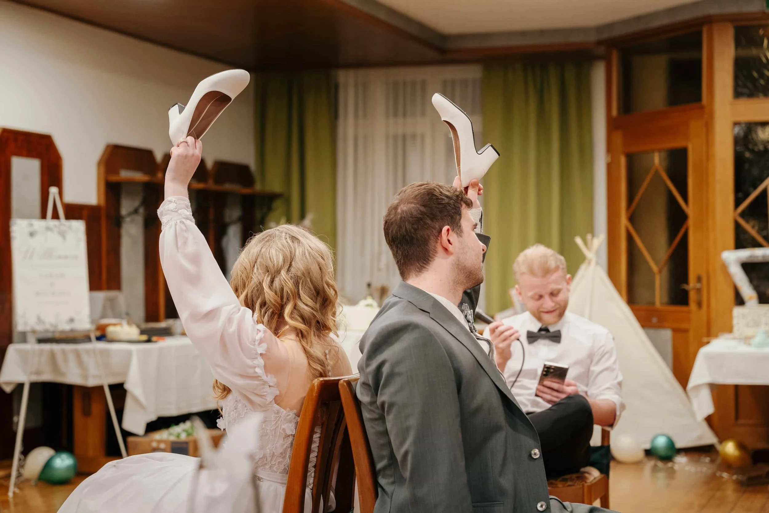 Ausgelassenes Schuhspiel bei der Hochzeitsfeier im Mostviertel, Braut und Bräutigam sitzen Rücken an Rücken und halten die weißen Brautschuhe hoch