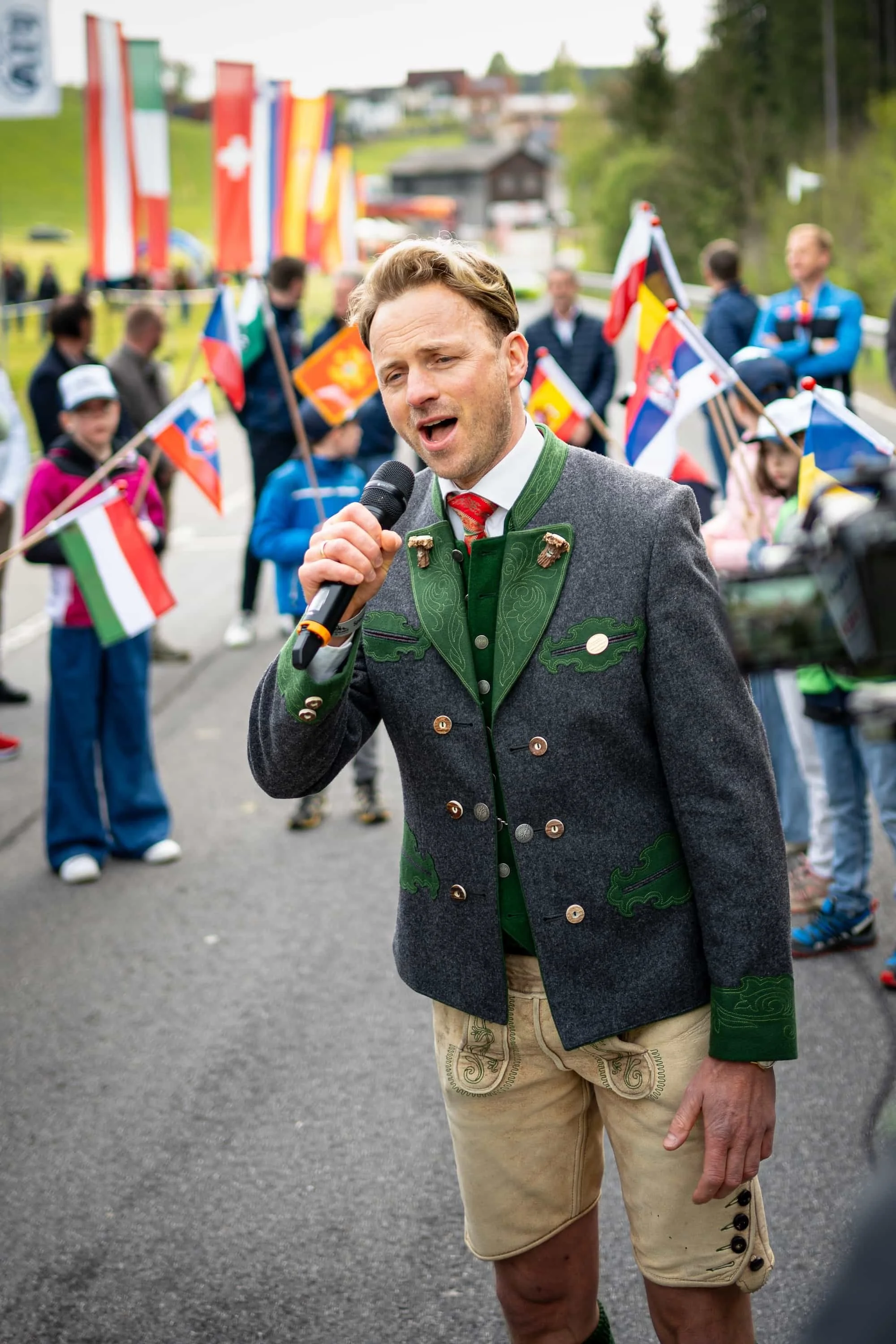 Musiker in traditioneller Tracht singt bei einer Veranstaltung in Österreich, im Hintergrund internationale Fahnen