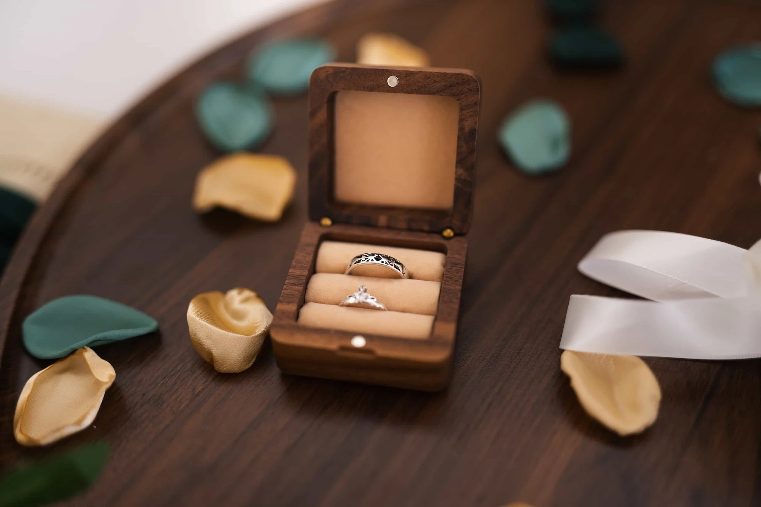 Eheringe in einer Ringbox aus Holz, umgeben von goldenen und grünen Blütenblättern