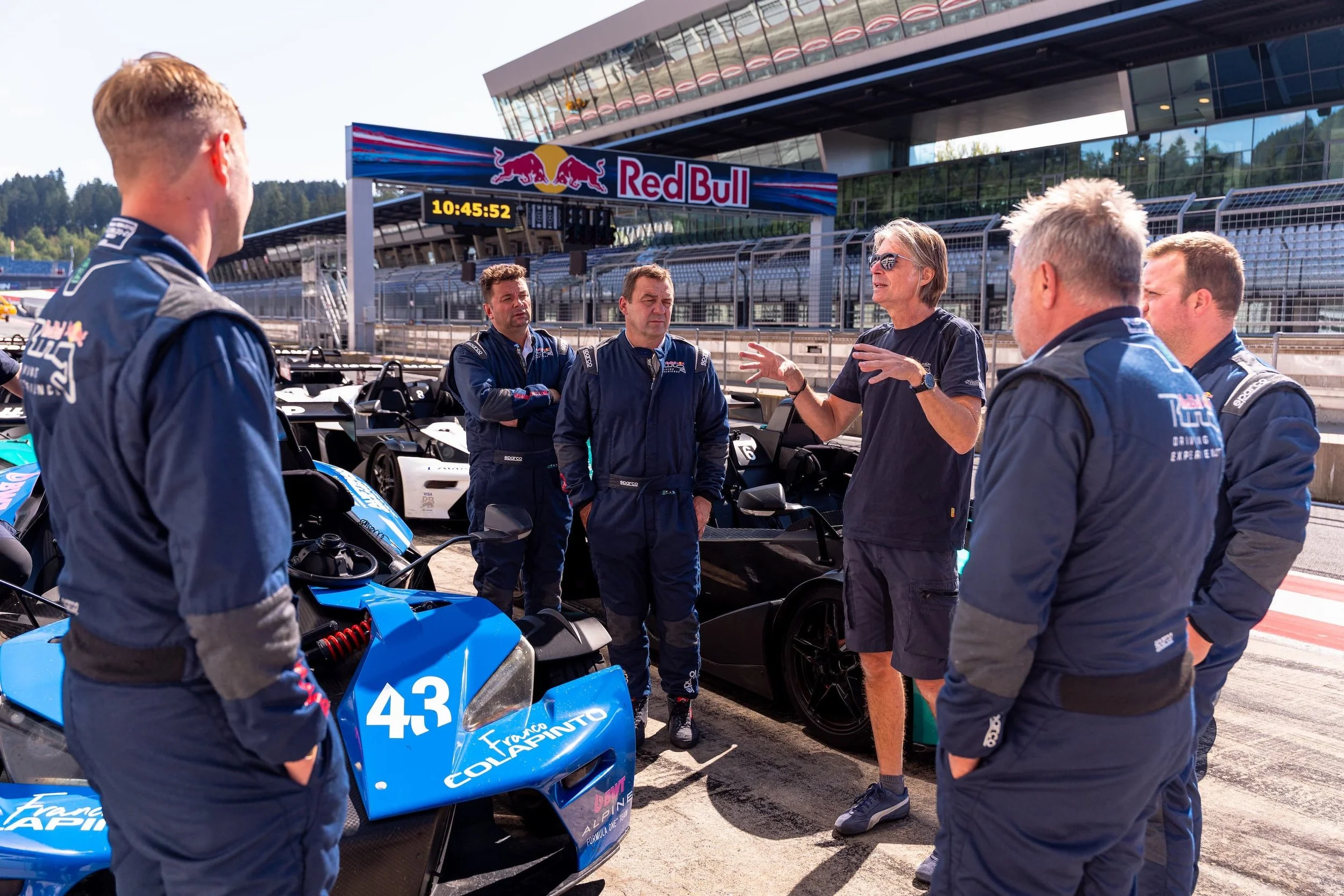 Instruktoren-Team der Red Bull Ring Driving Experience im Gespräch in der Boxengasse, im Hintergrund die KTM X-Bow Rennwagen und das Boxengebäude