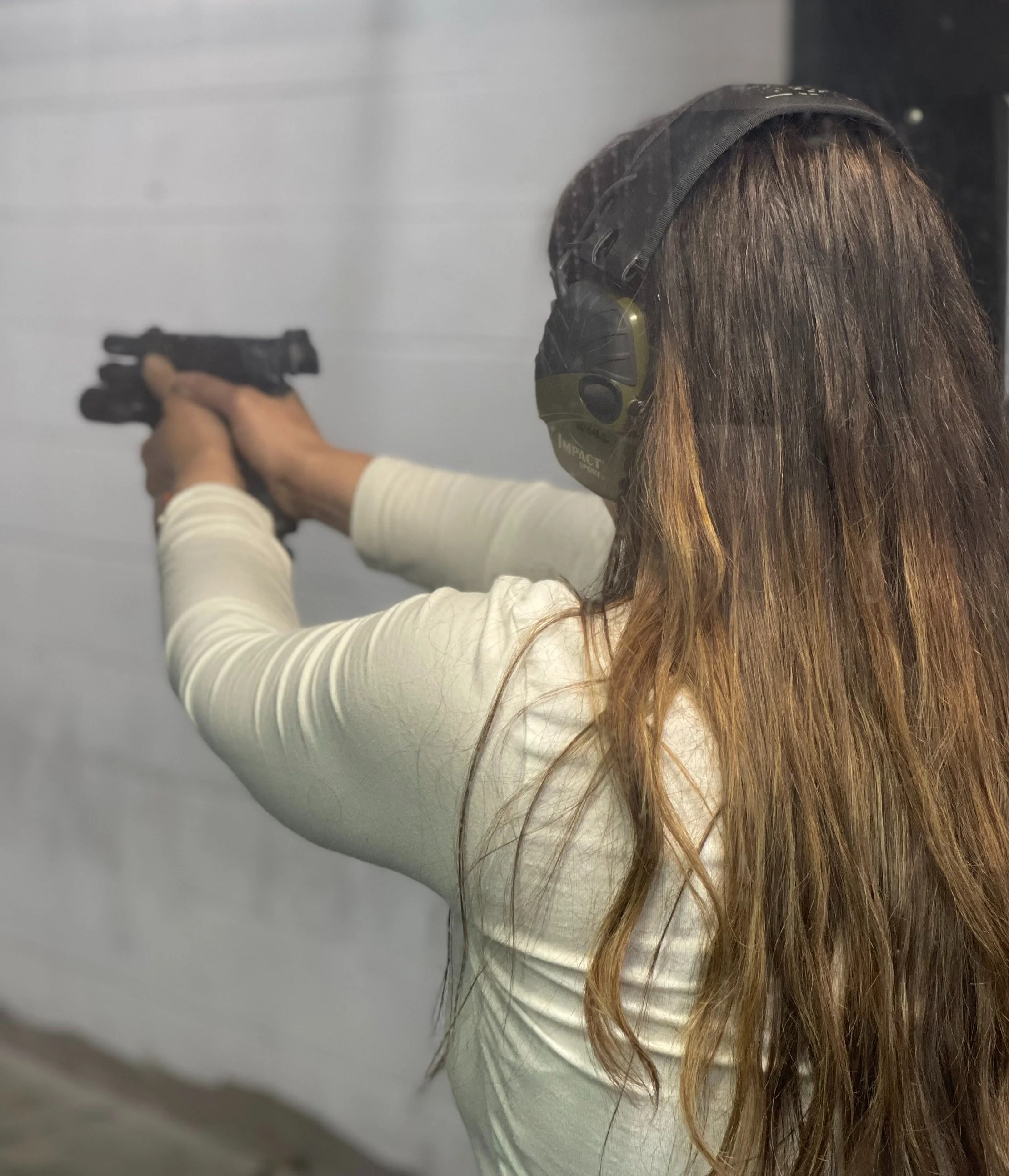 Person at a shooting range wearing headphones and holding a handgun, aiming forward. Interactive self-defense and corporate security training in a realistic shoot house environment at A+R Tactics.