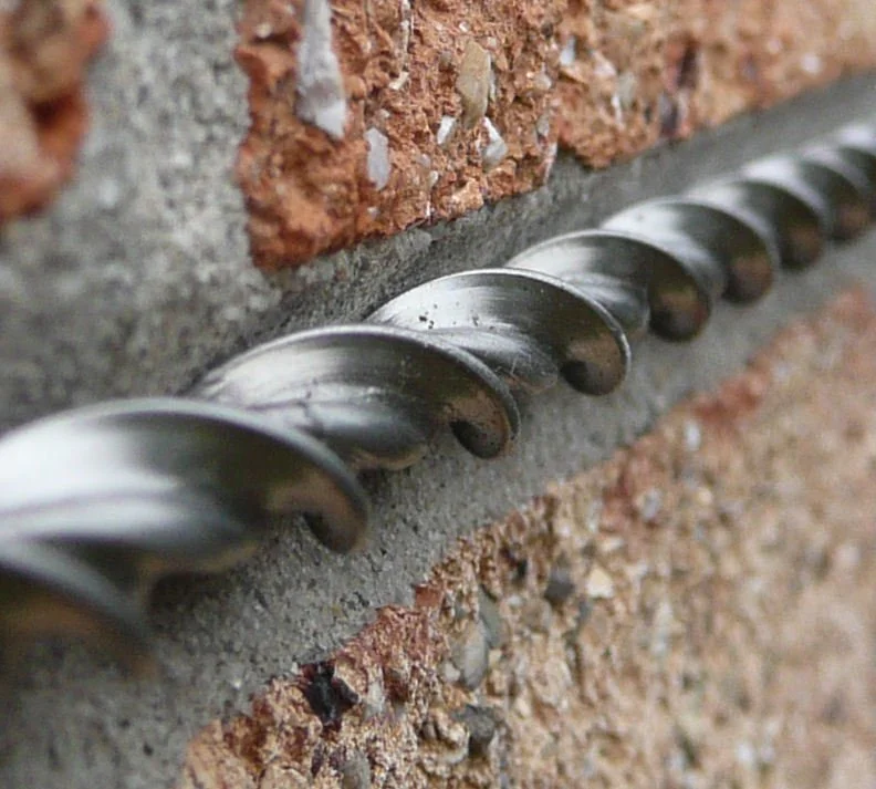 Close-up of a metal helical wire reinforcement embedded in a brick wall mortar joint.