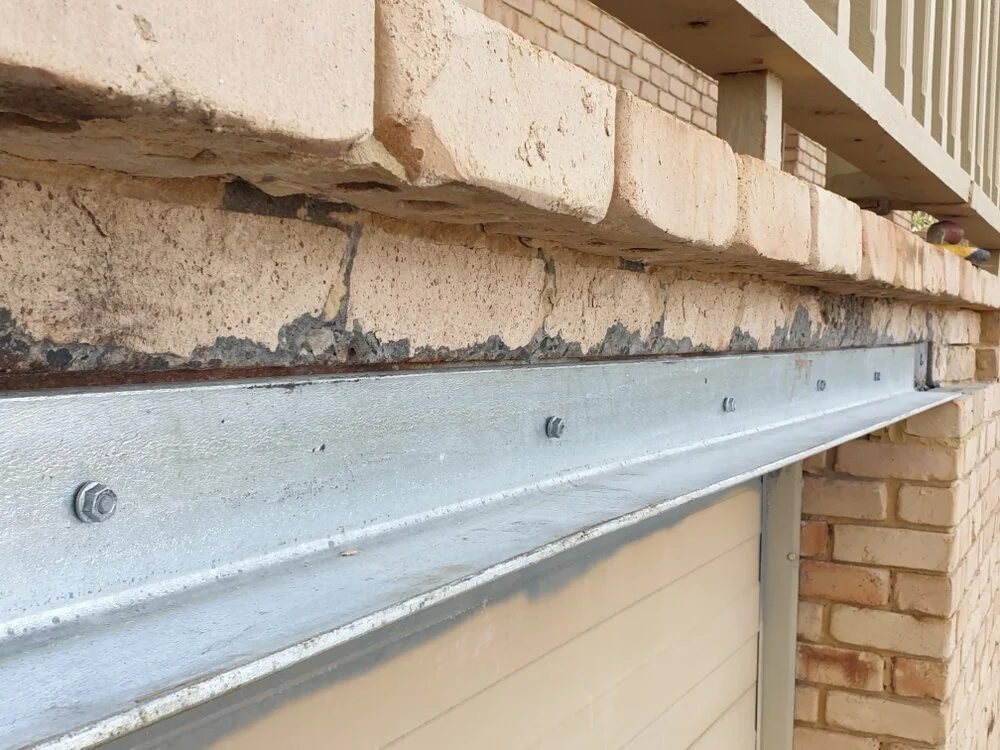 Close-up of brick wall with deteriorating mortar and metal support beam secured by bolts.