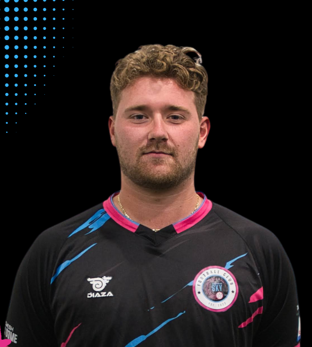 A young man with short red hair and a beard wearing a white and pink sports jersey inside an indoor soccer arena.