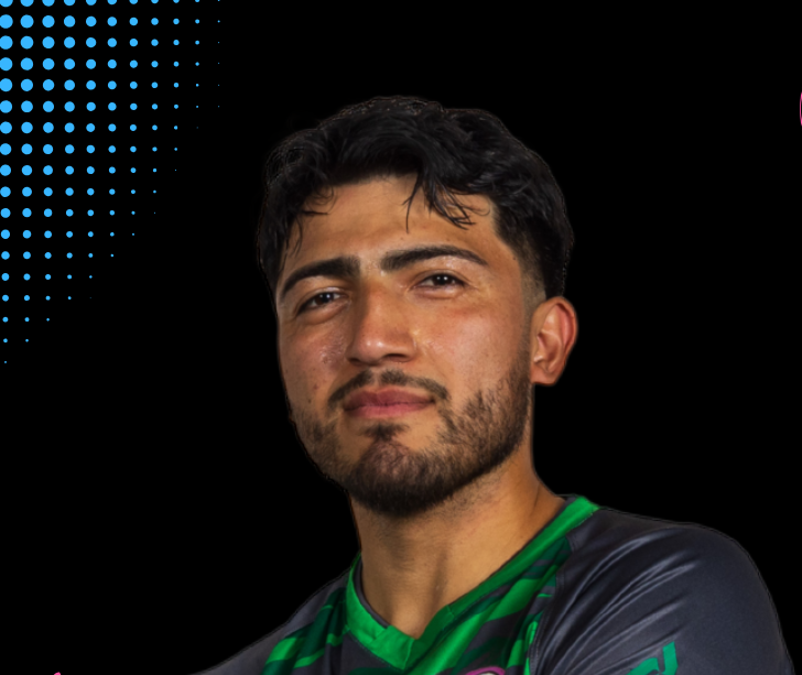 A young man with dark hair and a goatee holding a colorful soccer ball towards the camera in a sports facility.