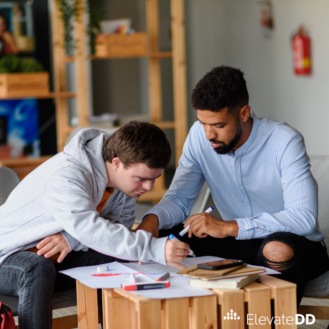 A teacher and student sit together at a small table to work on an assignment.