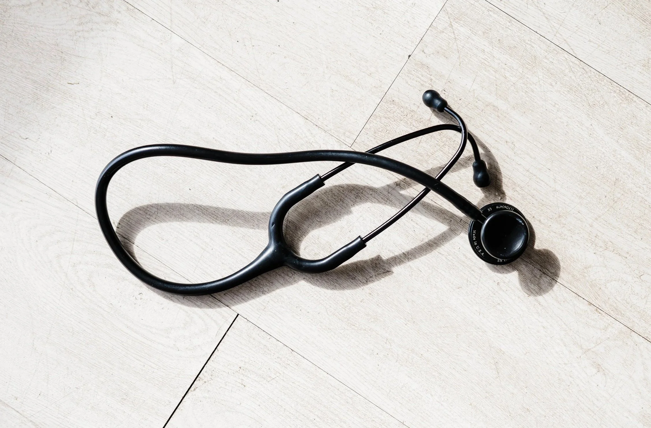 A woman wearing a white sports bra and gray zip-up hoodie stretching with arms raised on a dock near water at sunset.