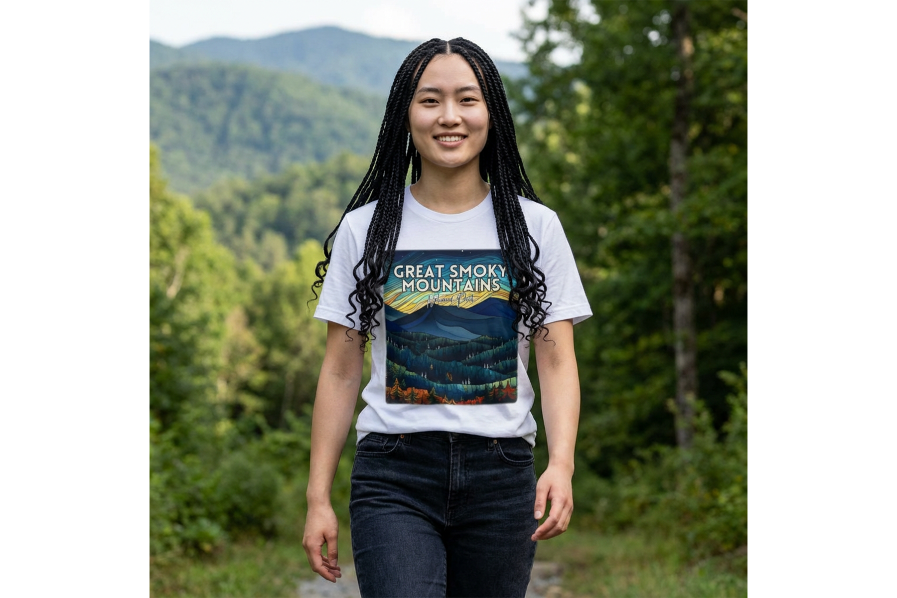 A young woman with long braided hair smiling while walking outdoors on a trail surrounded by trees and mountains in the background, wearing a white T-shirt with a colorful mountain graphic and the text 'Great Smoky Mountains'.