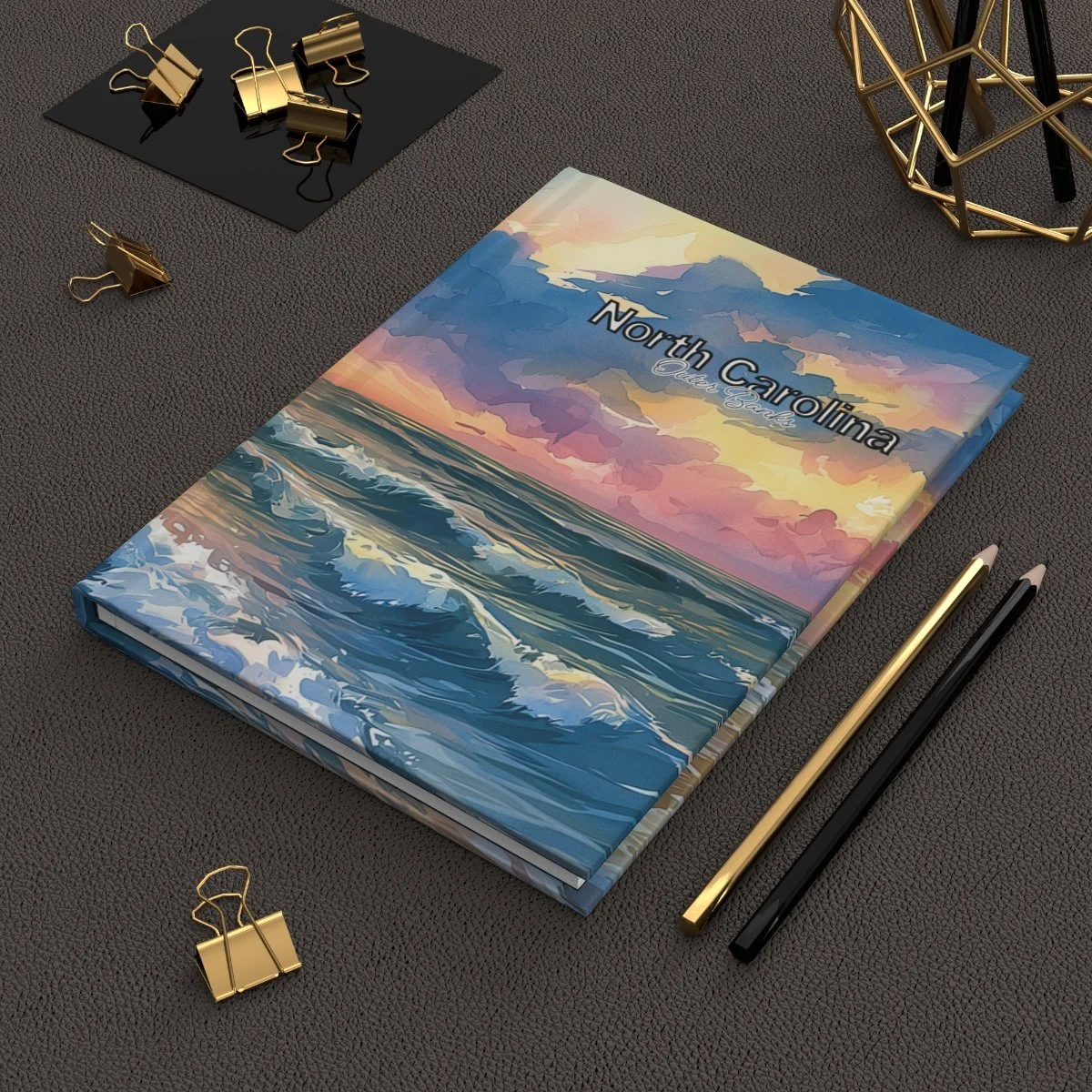 North Carolina coastal watercolor journal on a dark desk with gold clips and pens