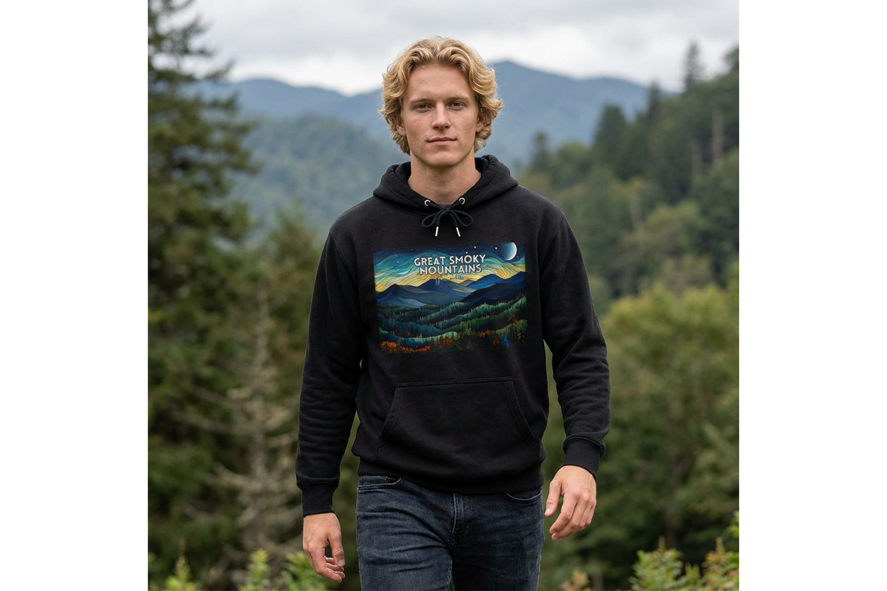 A young man with wavy blonde hair walking outdoors in a lush, green forested area with mountains in the background, wearing a black hoodie with a colorful mountain landscape graphic and the text 'Great Smoky Mountains'.