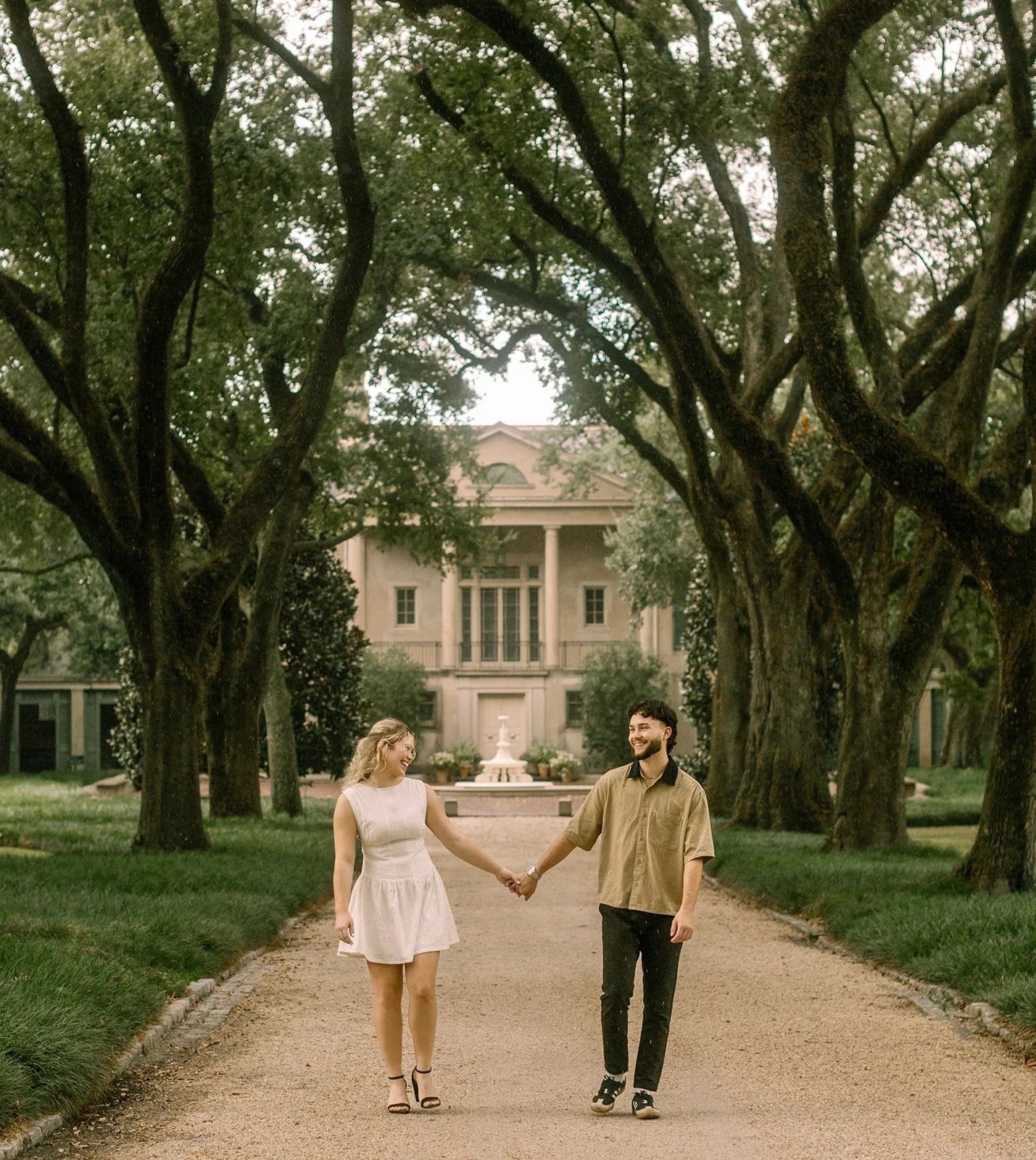 A couple walking at Longue Vue House and Gardens in New Orleans, moments before a surprise marriage proposal, surrounded by lush greenery and classic Southern architecture.