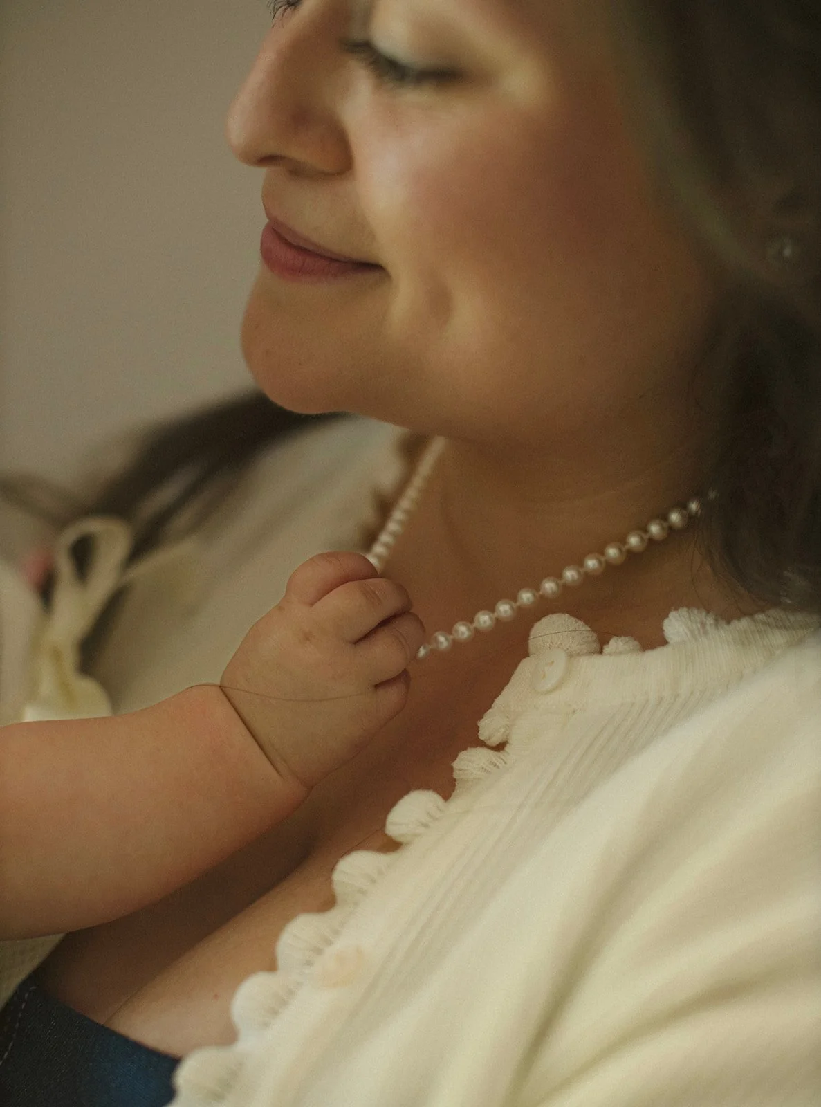 Close-up of a baby holding her mother's pearl necklace during an intimate family photo session.