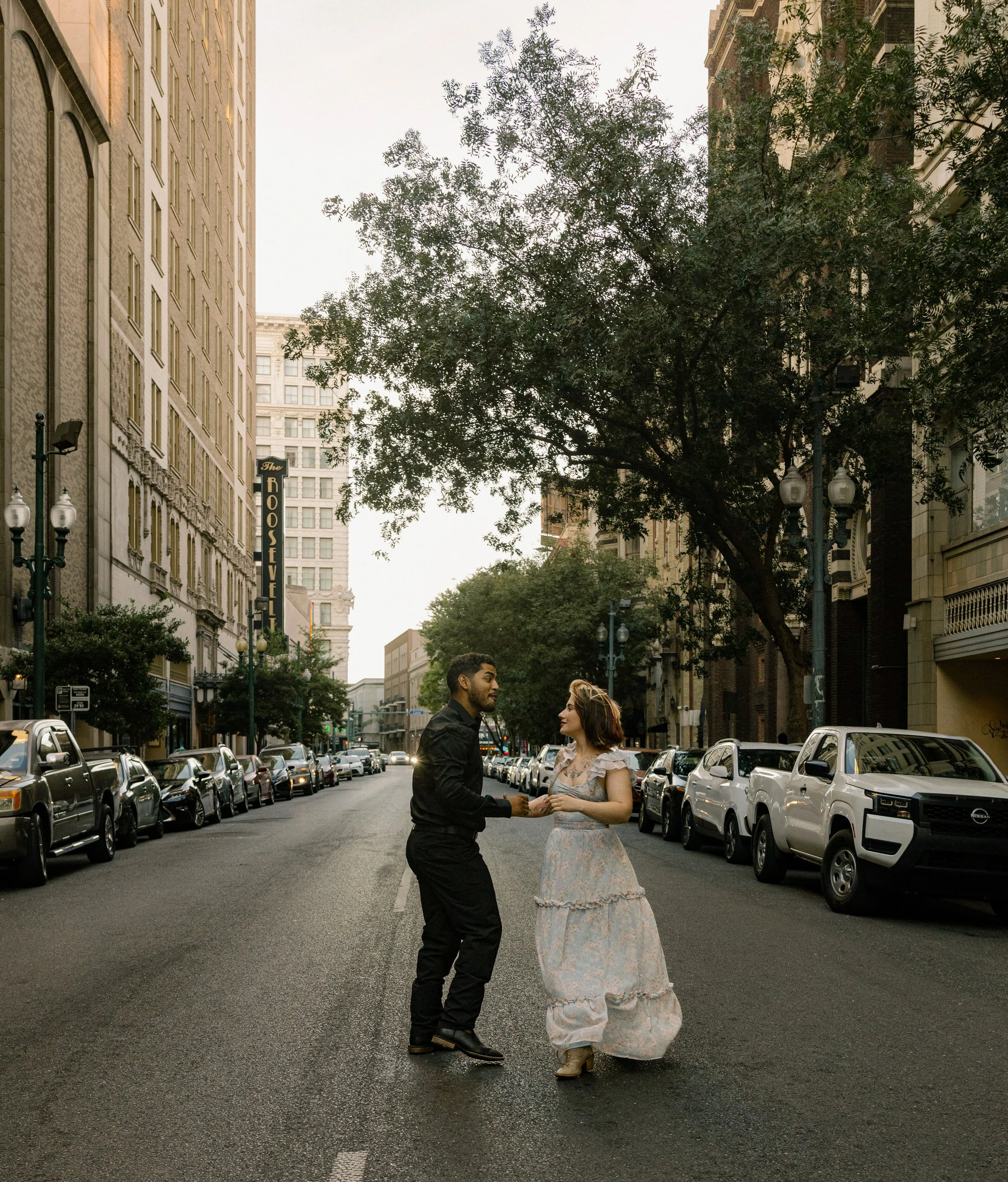 Couple dancing in the middle of a cobblestone street as the sun sets between the buildings.